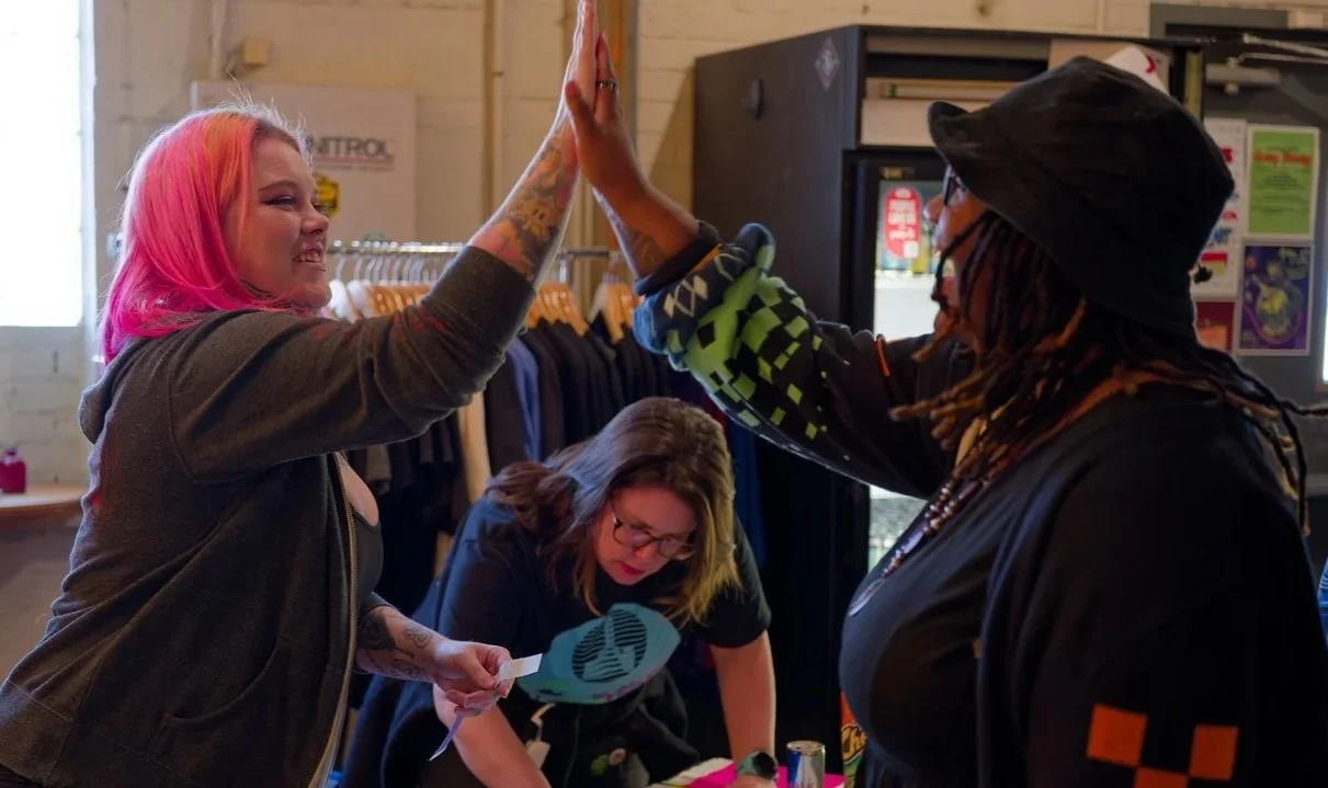 A person with pink hair and a person with dreads high fiving