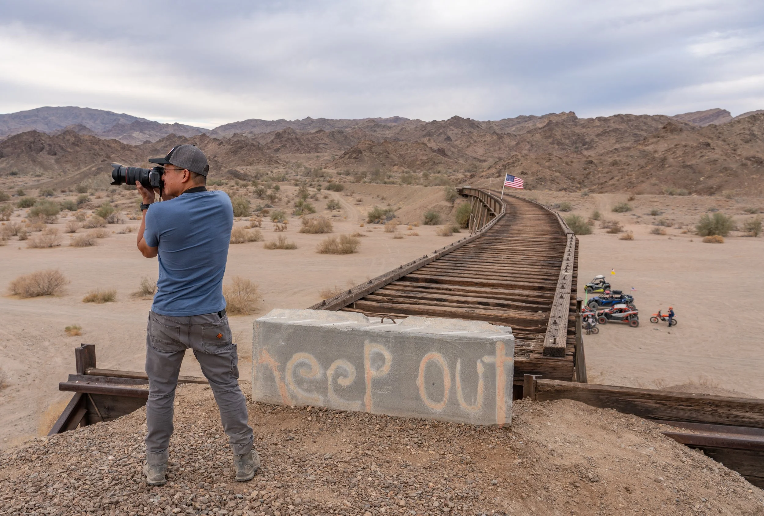 Me photographing near a desert railroad trestle with an American flag and 'Keep Out' graffiti. Photo taken by Ashwin Vasavada.