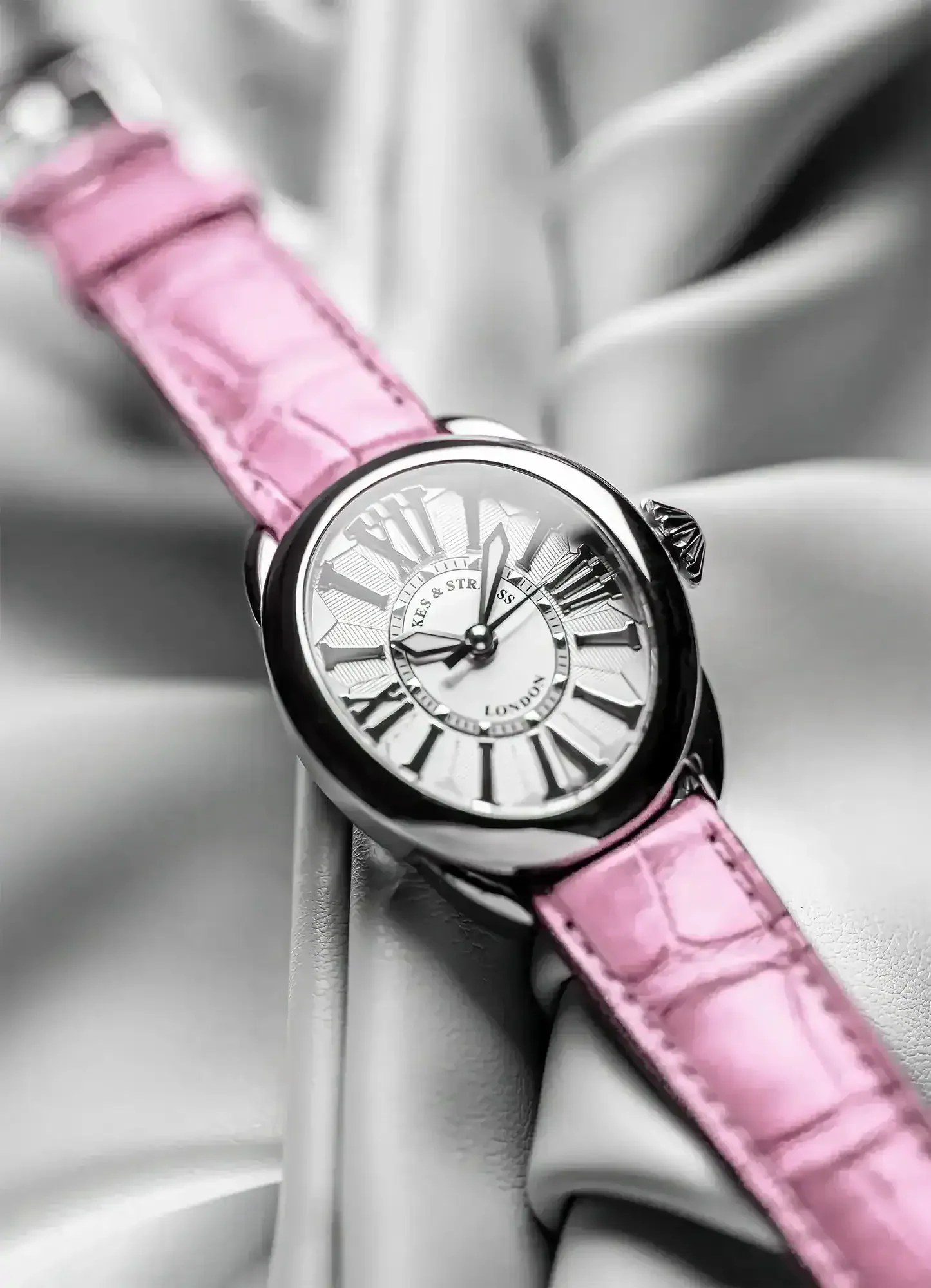 Regent women’s oval watch on the greay background, pink leather strap, polished steel case.webp