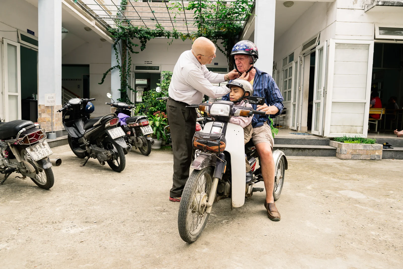 Matthew Keenan (68) is a friend of David, who also fought in Vietnam. He regularly travels from New York to Da Nang to visit the DAVA Center and publicizes the daily lives of Agent Orange victims on his Facebook page. Phuong Nguyen (39), a second generation victim of Agent Orange who works full-time in the DAVA Center, sits in front of him on the motorbike, while David helps to get ready for a ride. Supporting each other in moving on from the past has become the most important thing for the men.