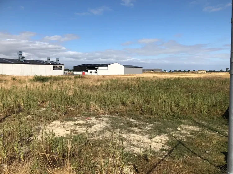 Grassy land at the Storage4Less Rolleston site before development, with neighbouring industrial buildings.