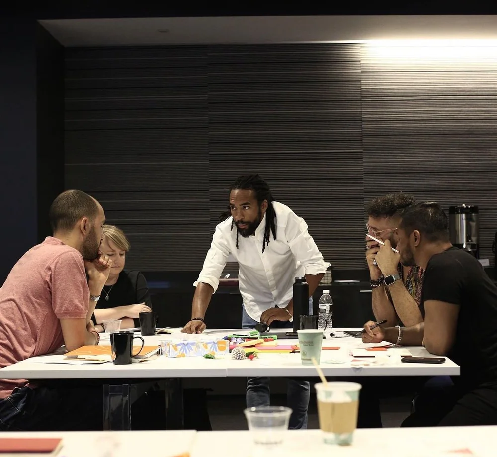 Didier Sylvain leaning over a table working with a group of five in a panelled meeting room