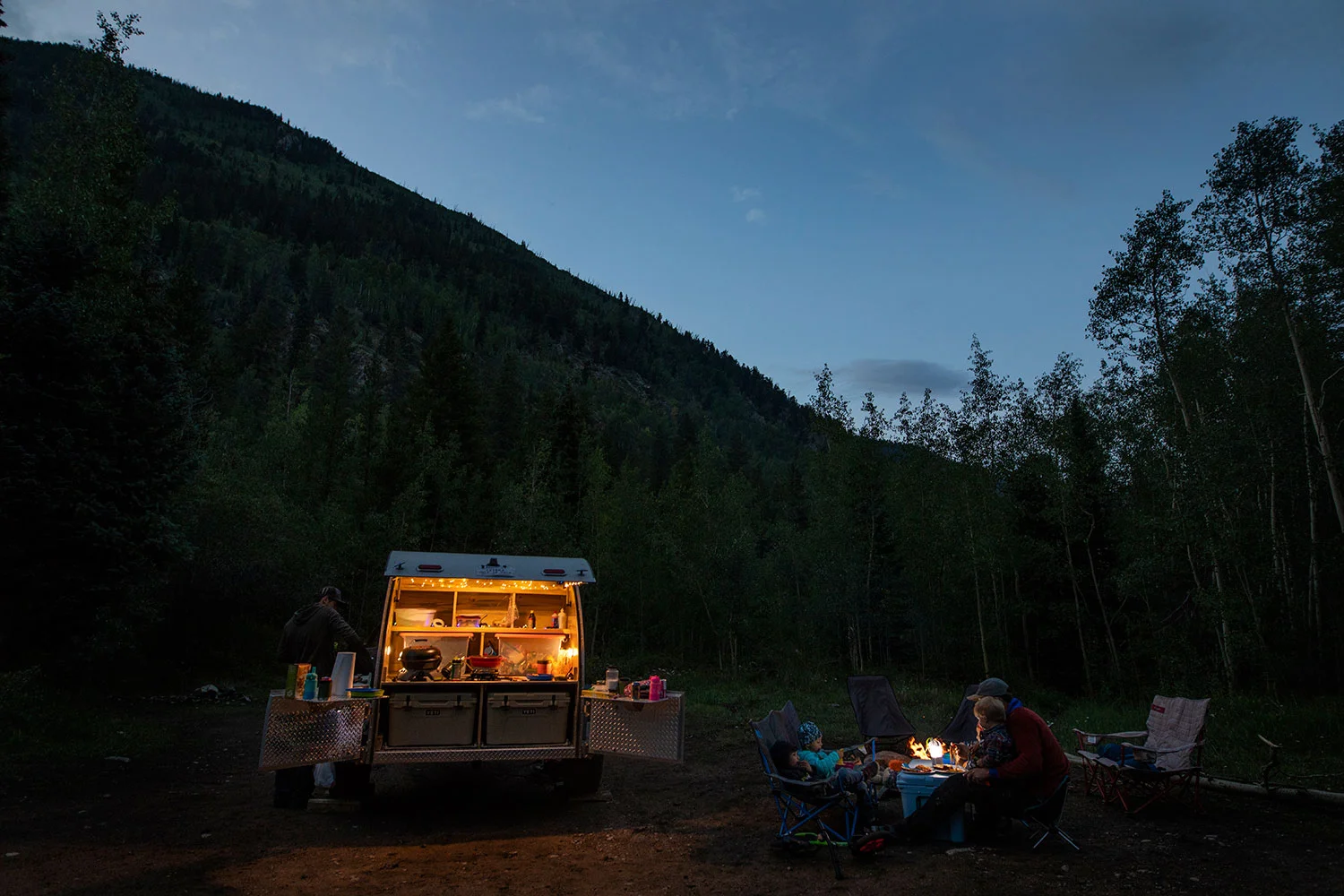 Family camping with teardrop trailer at night in the mountains