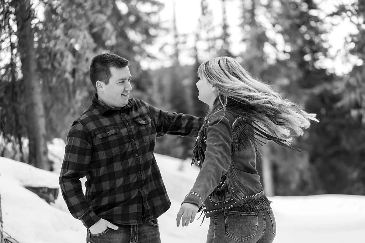 A black and white image of a couple dancing in the snowy woods for their engagement session.