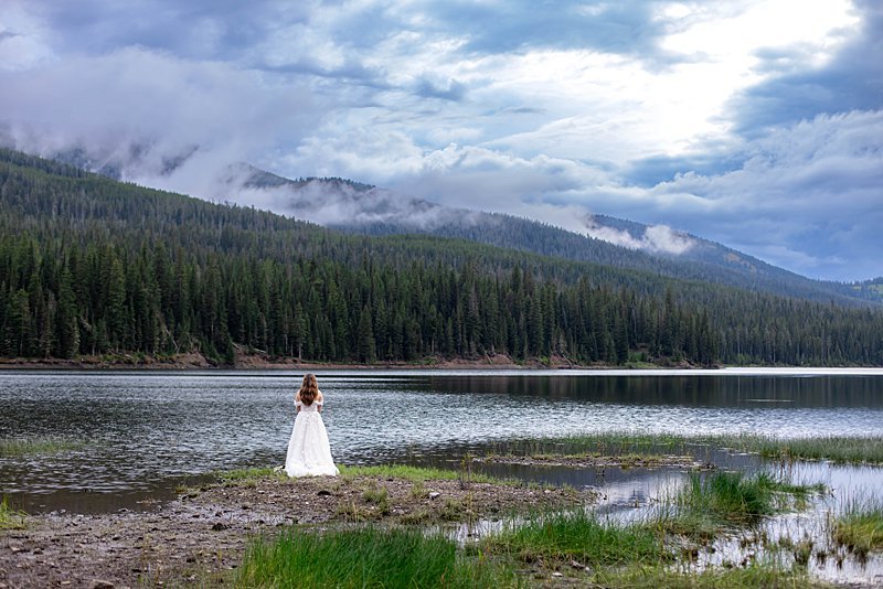 A bride in her wedding gown fly fishing along a reservoir deep in the mountains of Montana.
