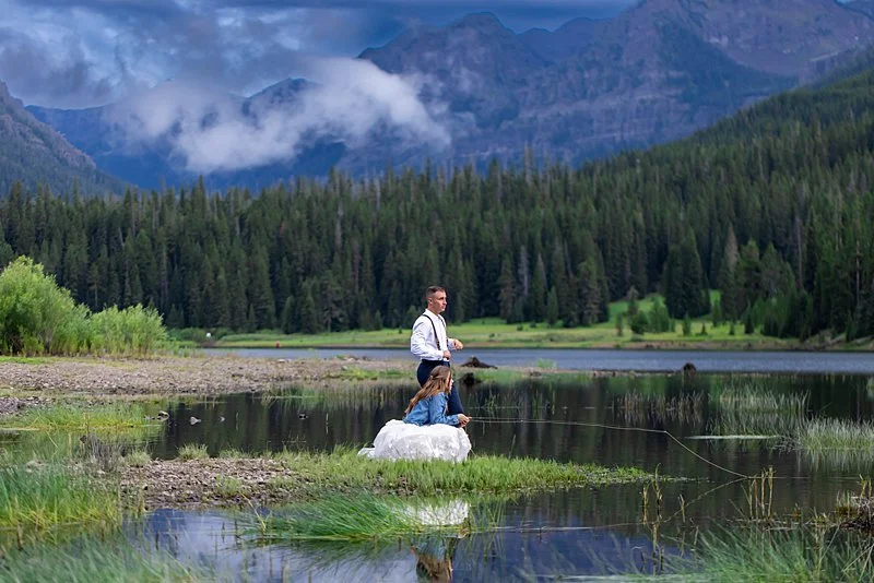 A couple wearing their wedding outfits flyfishing in quiet waters surrounded by Montana's Gallatin Range Mountains.