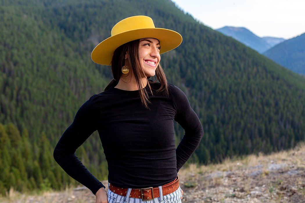 A Senior girl, in her cute yellow hat, on a mountain top to create fun and memorable senior portraits