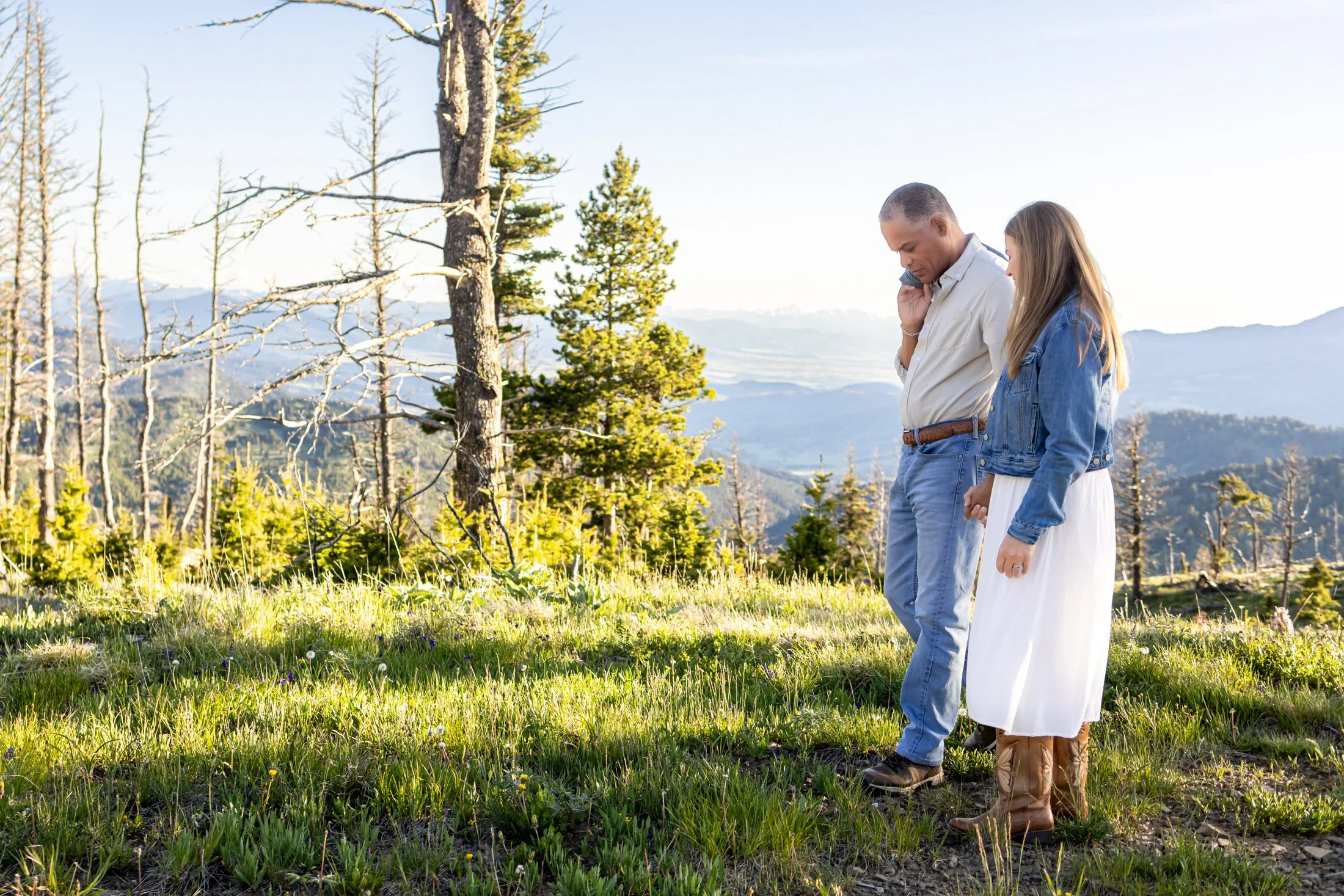 A mixed race couple, walking from camera right to left, on an overlook in the Montana mountains. They are holding hands and completely engaged with each other and relaxed as the camera captures a quiet moment between them.