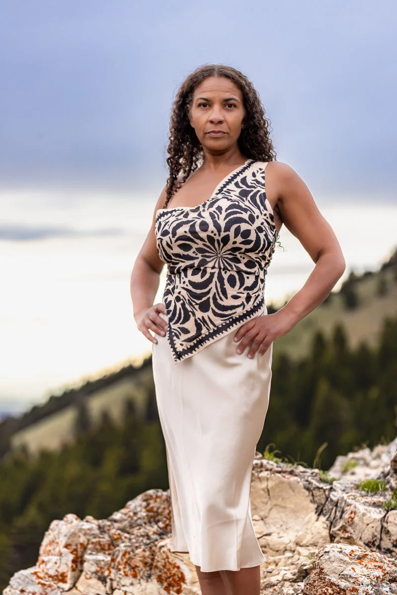 Woman standing on a mountain top, dressed for business, in a powerful hands on hips pose, ready to take on the world. The perfect reflection of her personal brand.