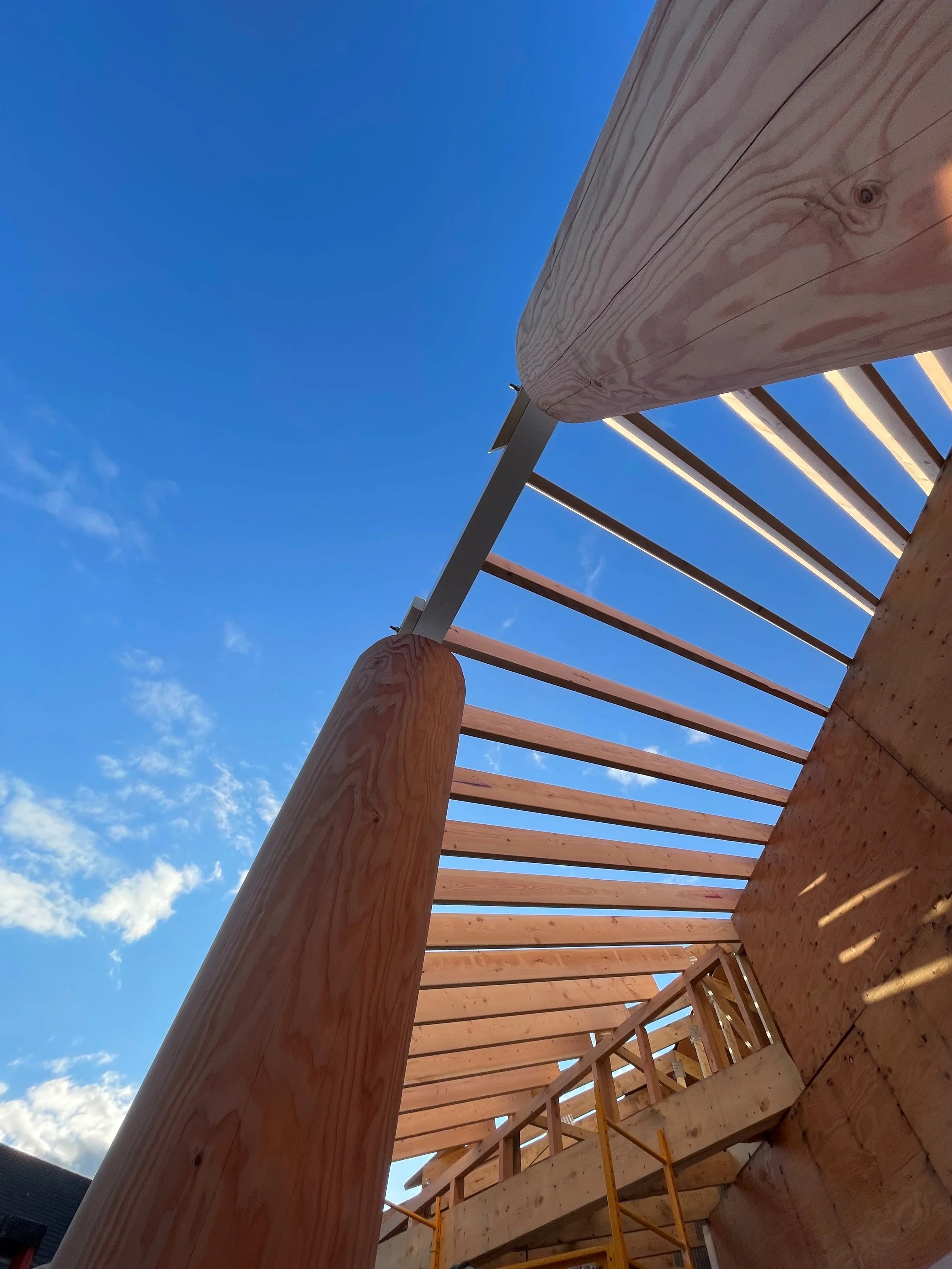 Low-angle view of a wooden structure under construction with a clear blue sky in the background.