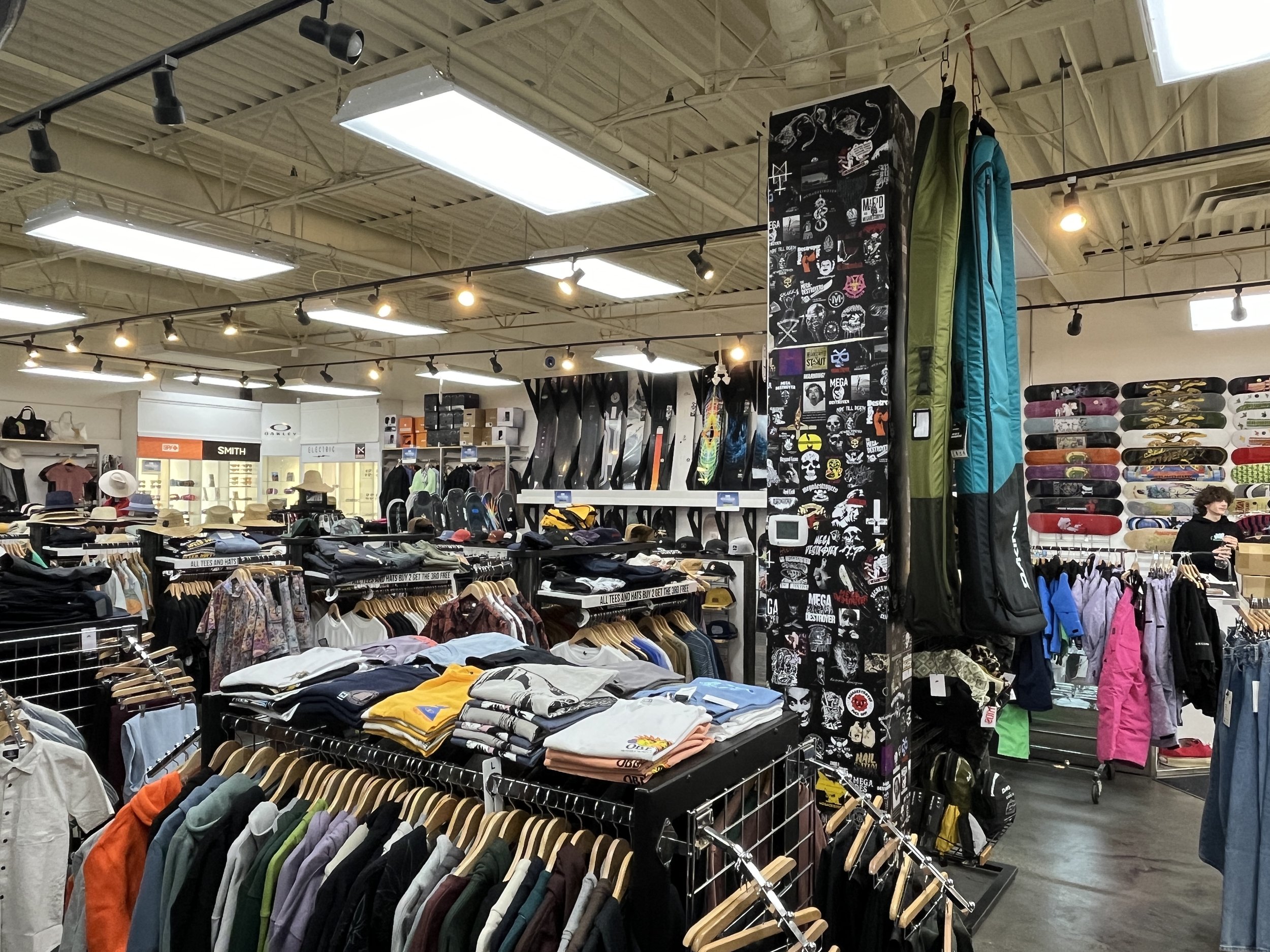 Inside a retail store with clothing racks, skateboards, and outdoor gear, illuminated by bright overhead lights.