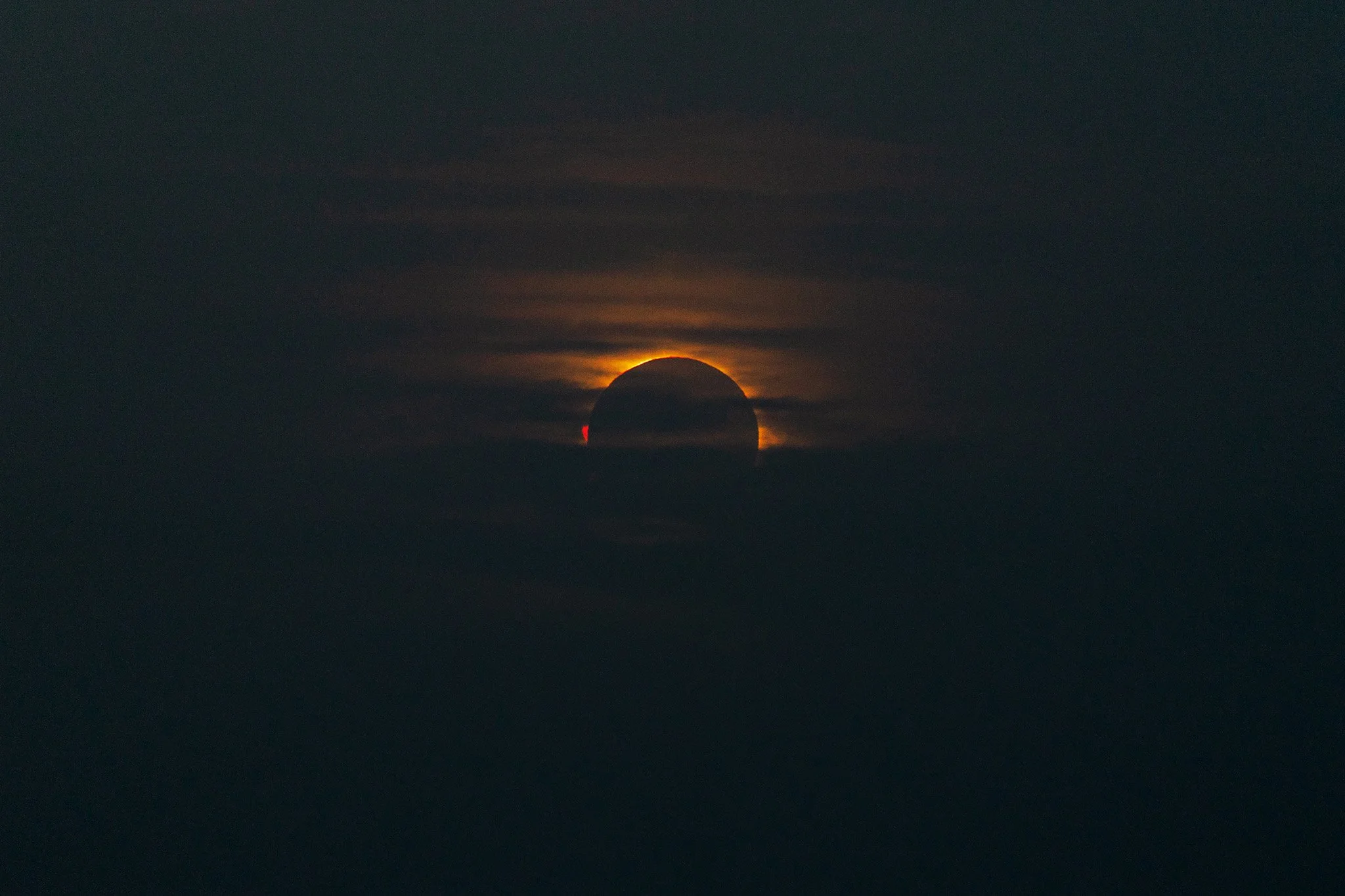The 2026 total solar eclipse with a pink solar prominence on the left side and some yellow/orange clouds surrounding it as photographed from Menorca, Spain.