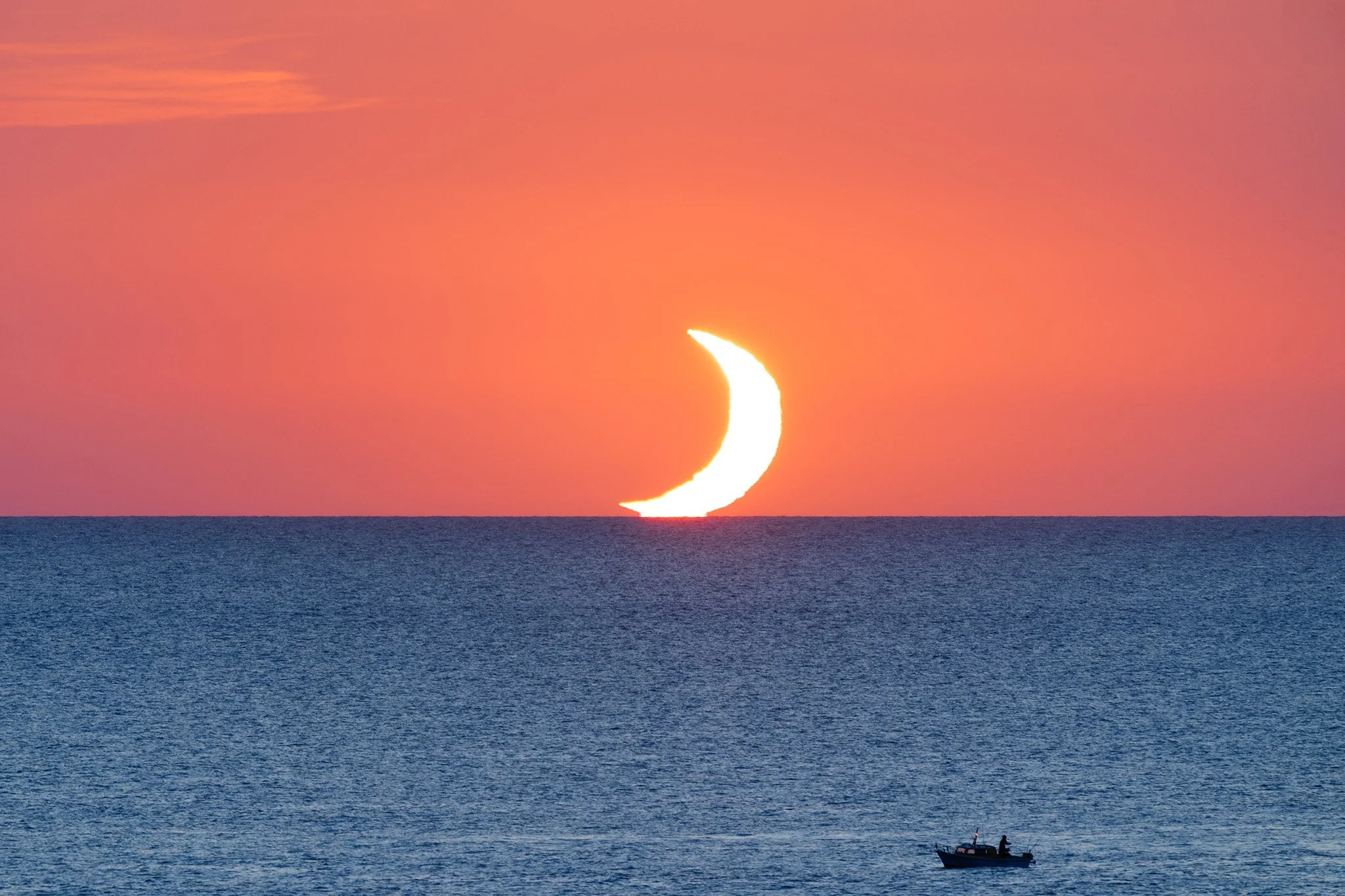 The partial solar eclipse sets into the Mediterranean Sea at sunset with a small boat in the foreground during the 2026 total solar eclipse as photographed from Menorca, Spain.