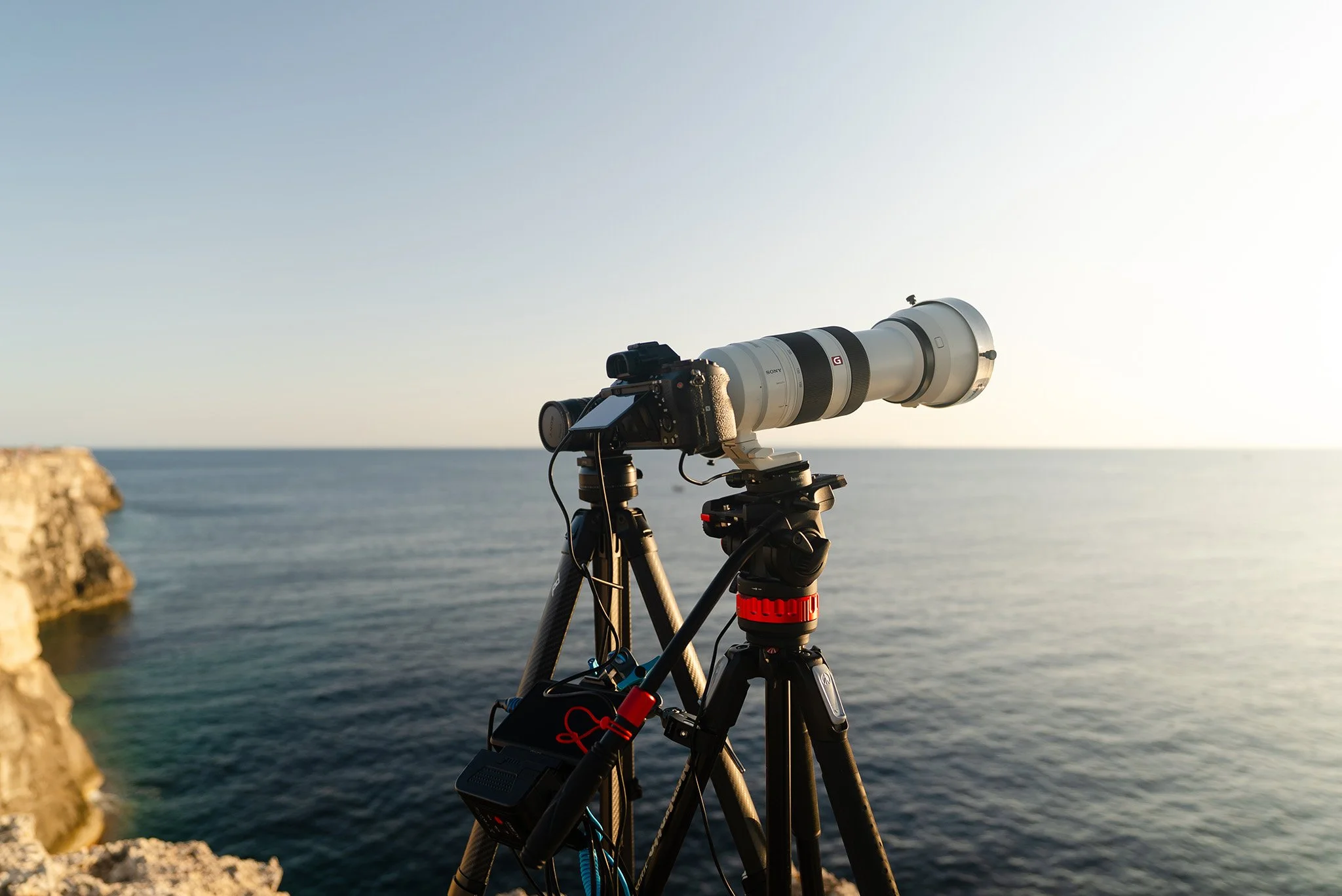 A Sony Alpha camera and a telephoto lens on a tripod with the Mediterranean Sea in the background taken in Menorca, Spain in preparation for the 2026 total solar eclipse.