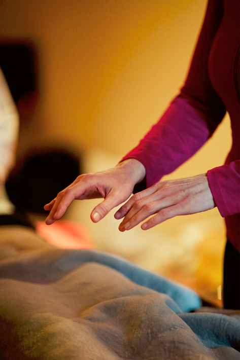 Close-up of a person performing a healing or massage therapy on a patient lying on a bed.