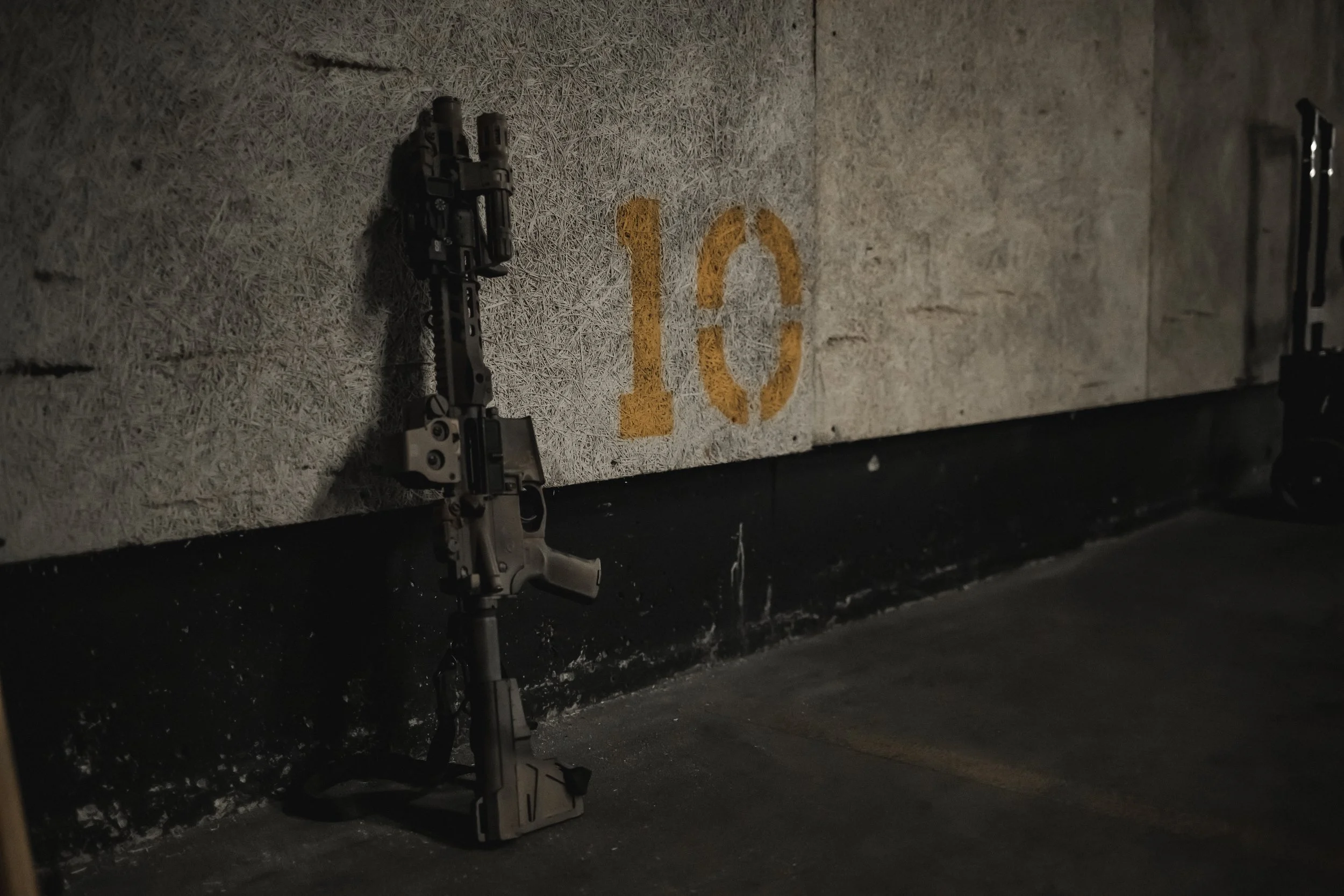 A handgun leaning against a concrete wall with a yellow "10" painted on it, in a dimly lit environment.