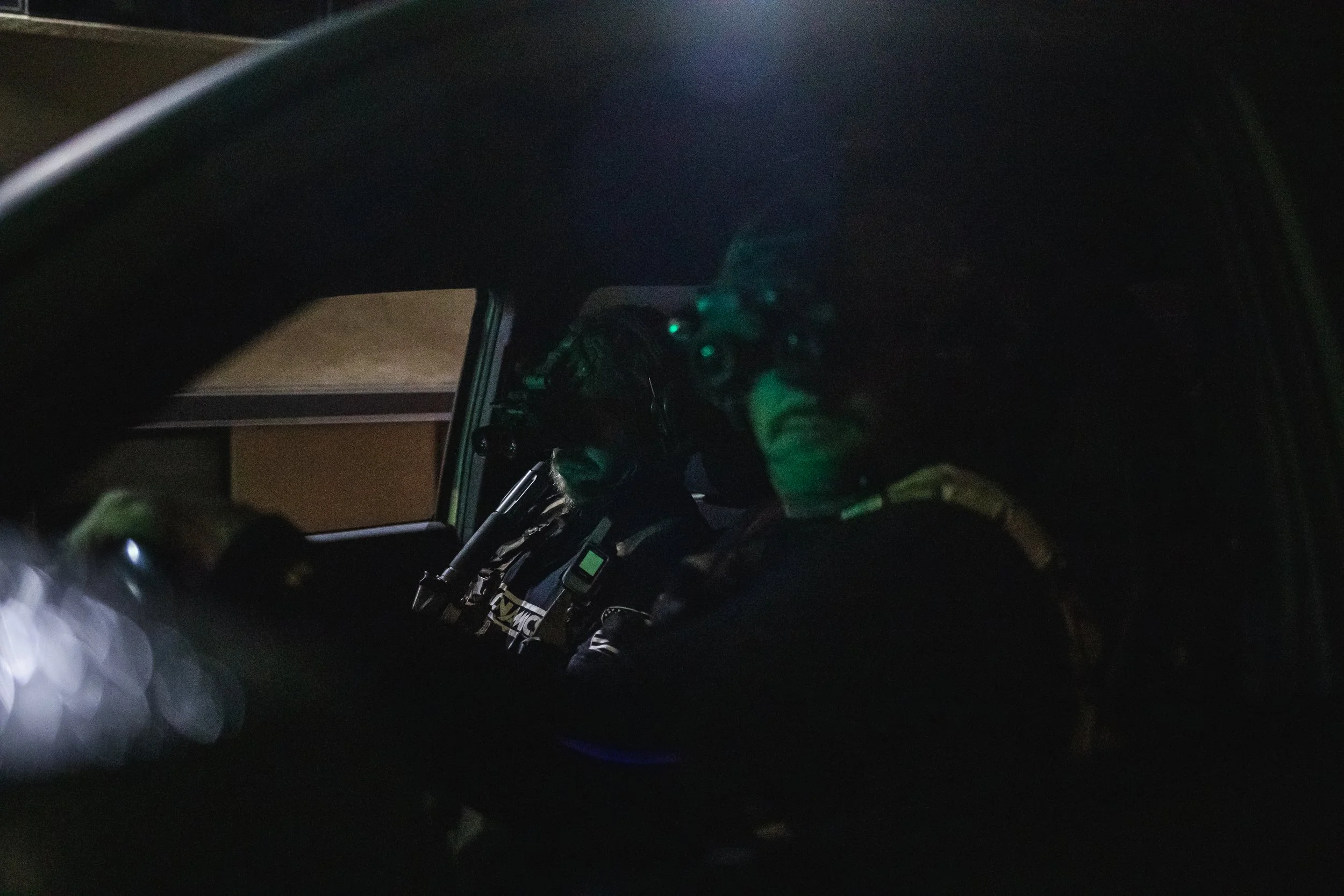 A person wearing a helmet and glasses sitting in the driver's seat of a dark vehicle at night.