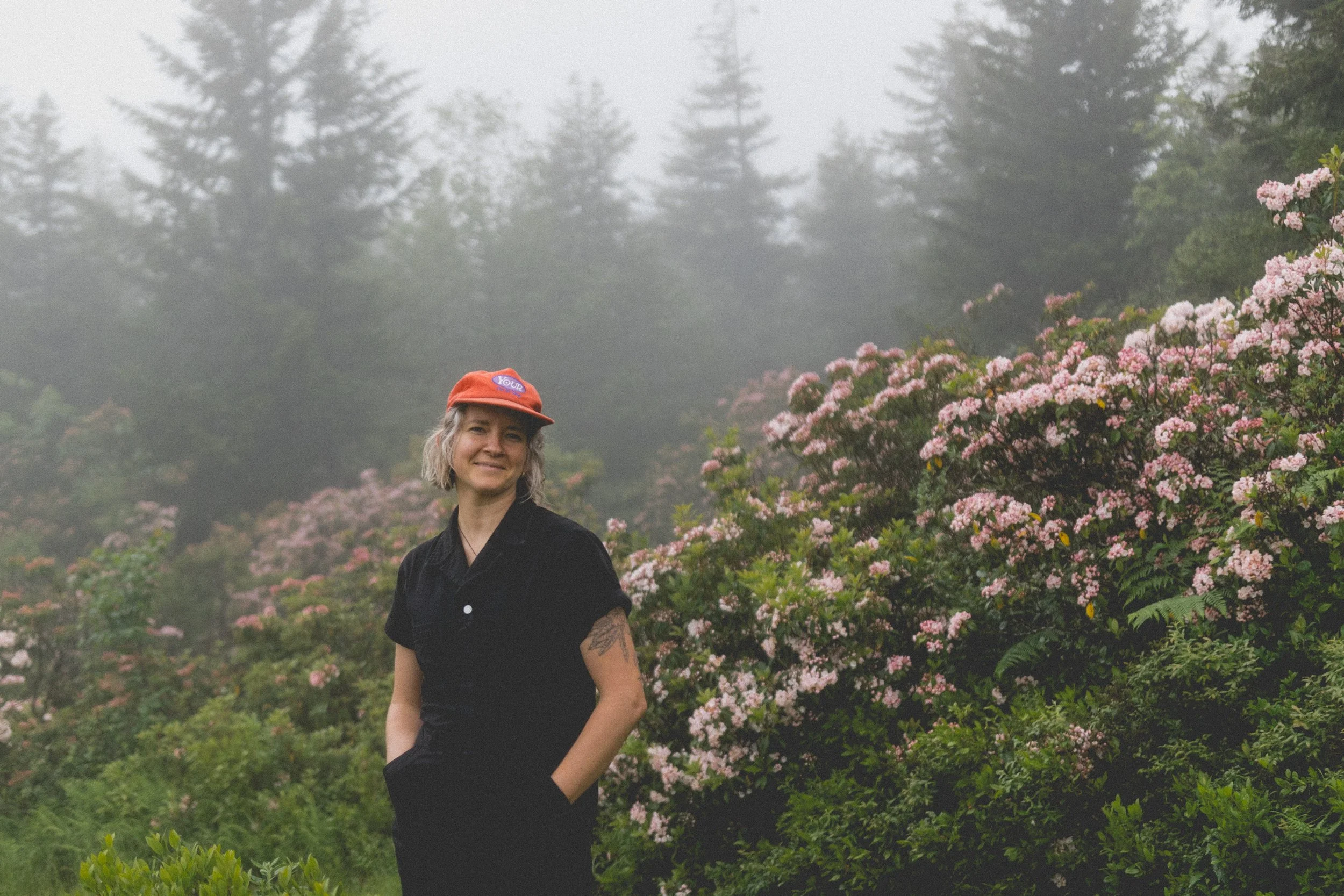 Braiden Maddox, an elopement videographer, poses in front of pink spring flowers at Dolly Sods in West Virginia.