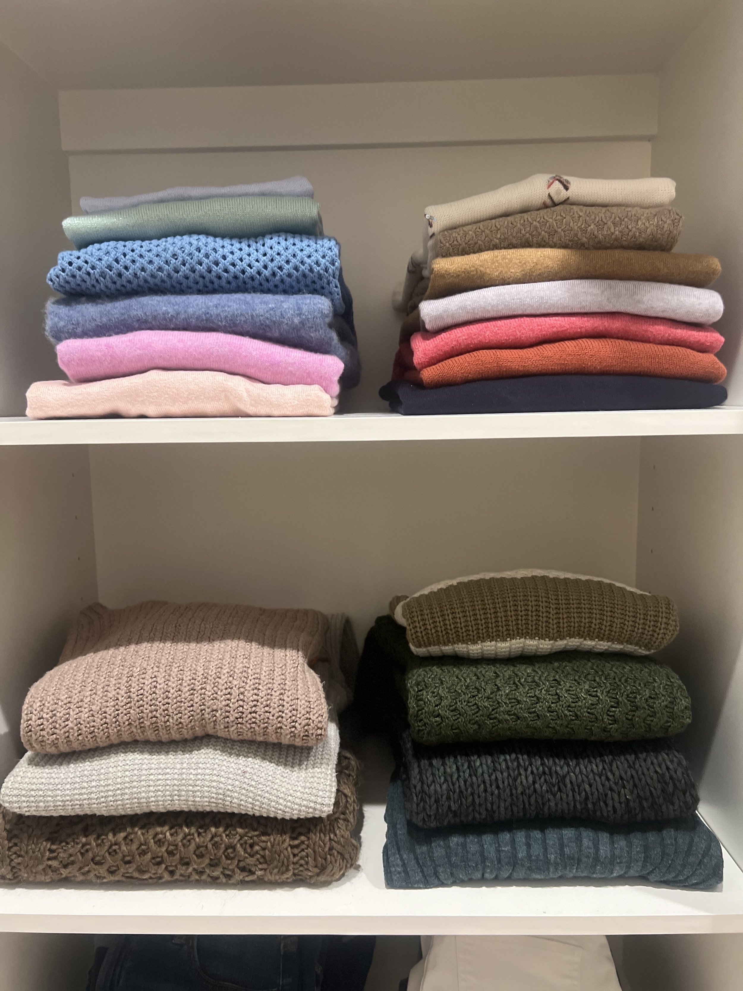 Stacks of folded sweaters and knitwear arranged on white shelves in various colors and textures.