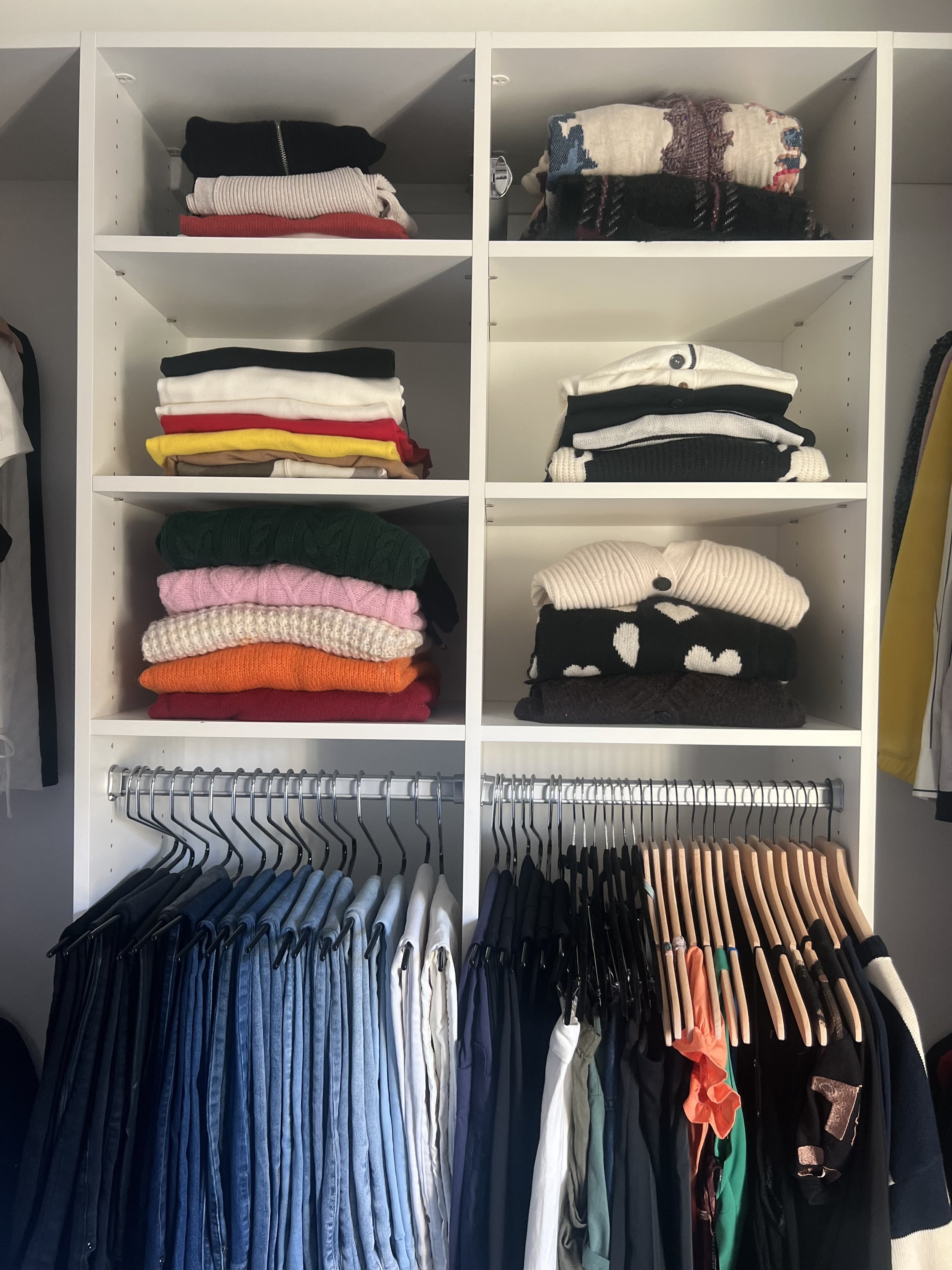 White closet with folded clothes on shelves and hanging shirts and pants on rods.