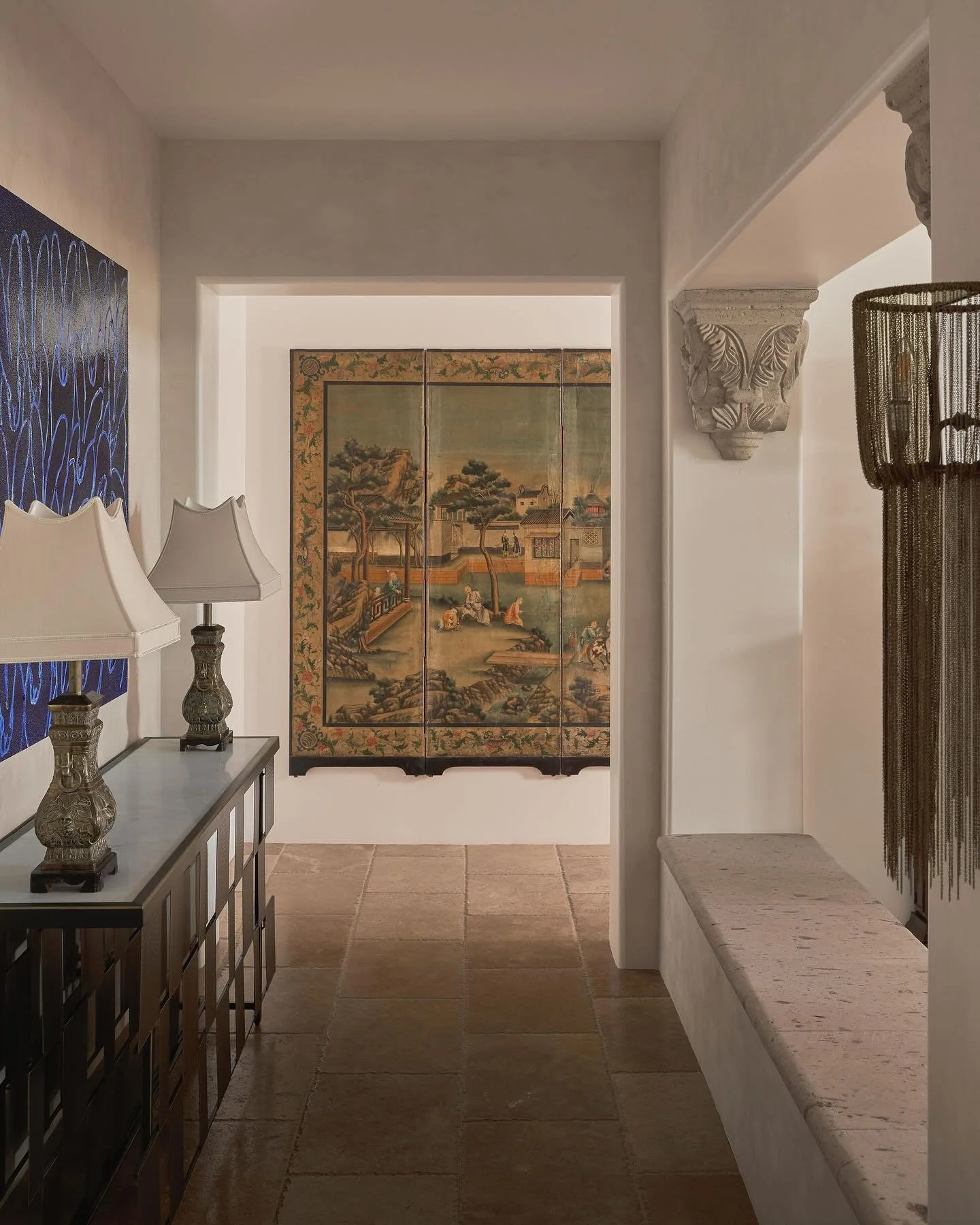 A quiet dialogue between past and present. An antique Chinese screen whispers stories of another time, contrasted by the playful charm of Hunt Slonem’s bunnies. Vintage lamps rest over a sleek stone-and-metal console, while cascades of metal ch