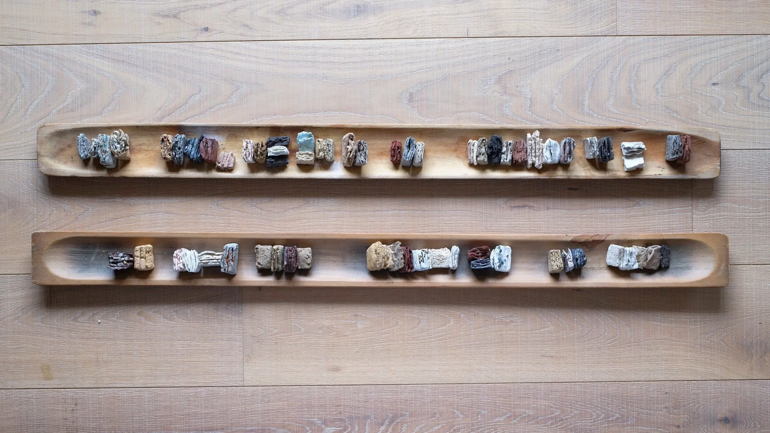 Three wooden trays with various small rock and mineral specimens on a wooden surface.