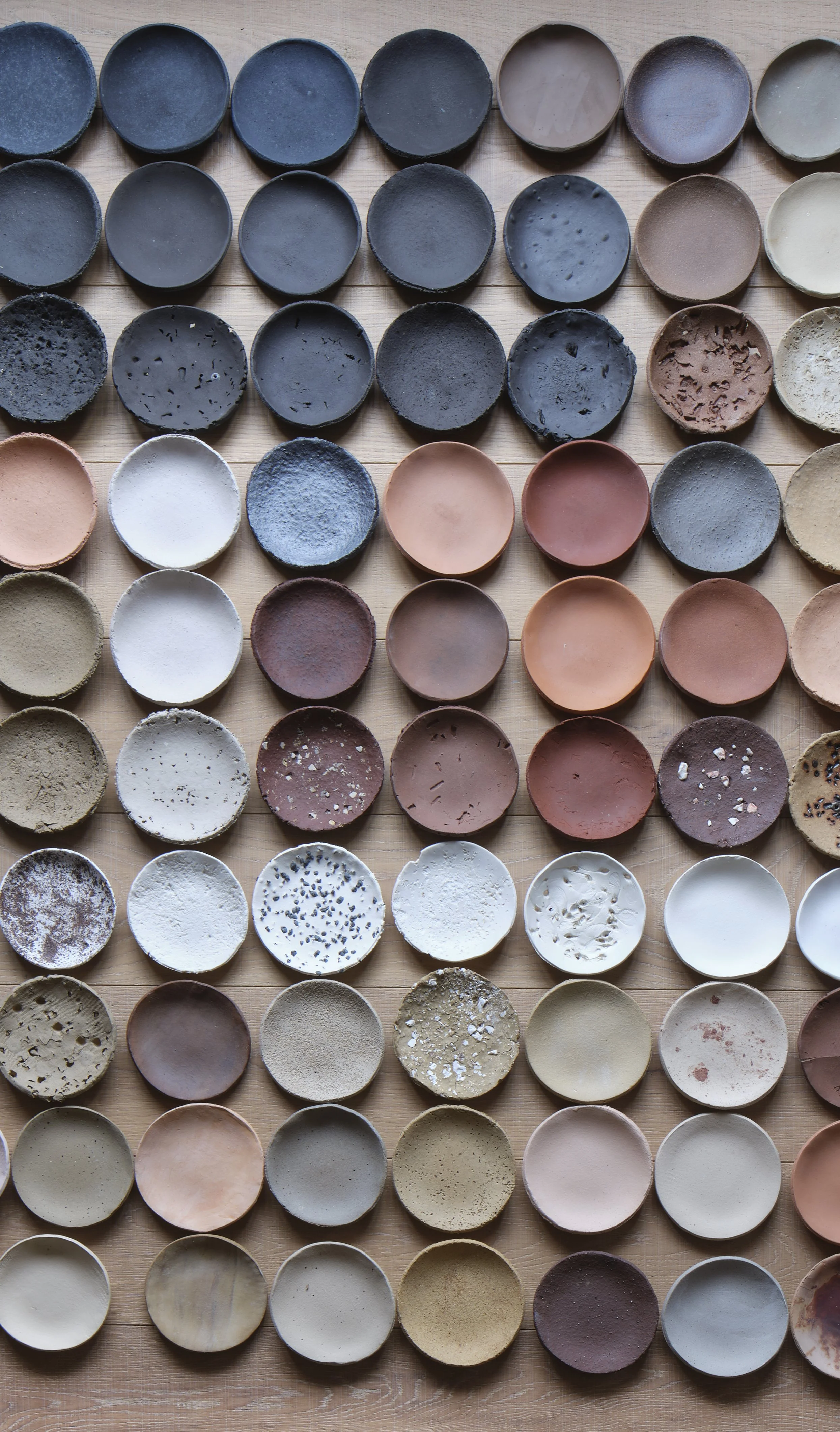 A collection of ceramic bowls arranged in rows on a wooden surface, showcasing various colors, textures, and finishes.