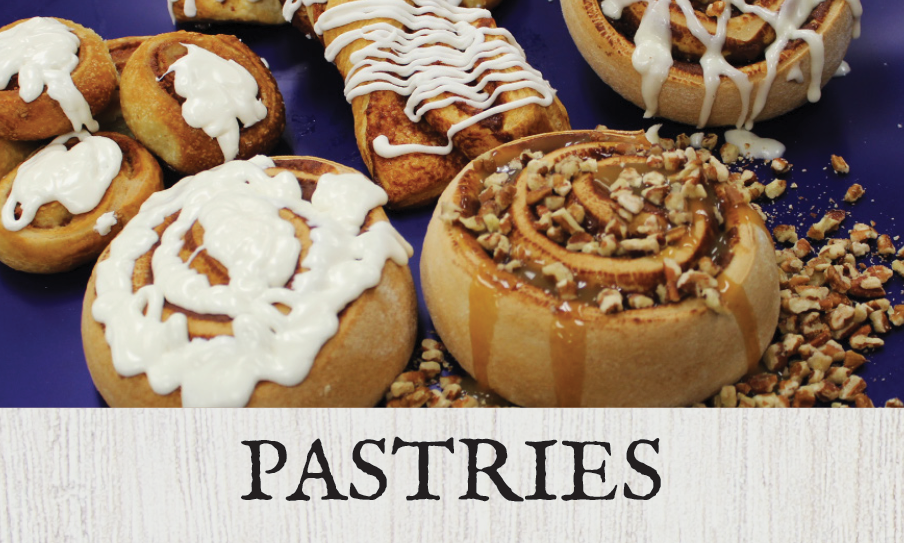Assorted cinnamon rolls and pastries with icing and nuts on a plate with a "PASTRIES" sign underneath.