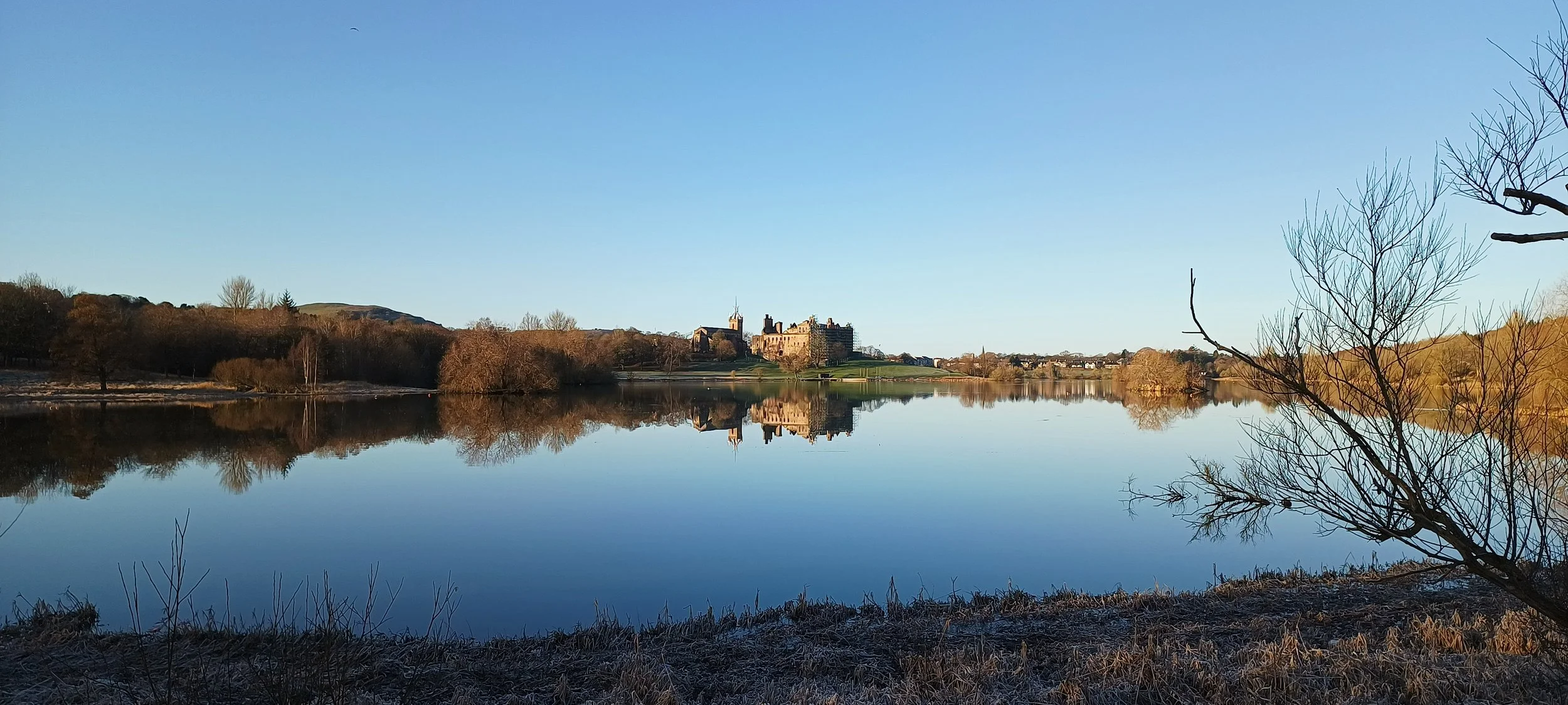 View across Linlithgow Loch towards Linlithgow Palace, reflected in the water.