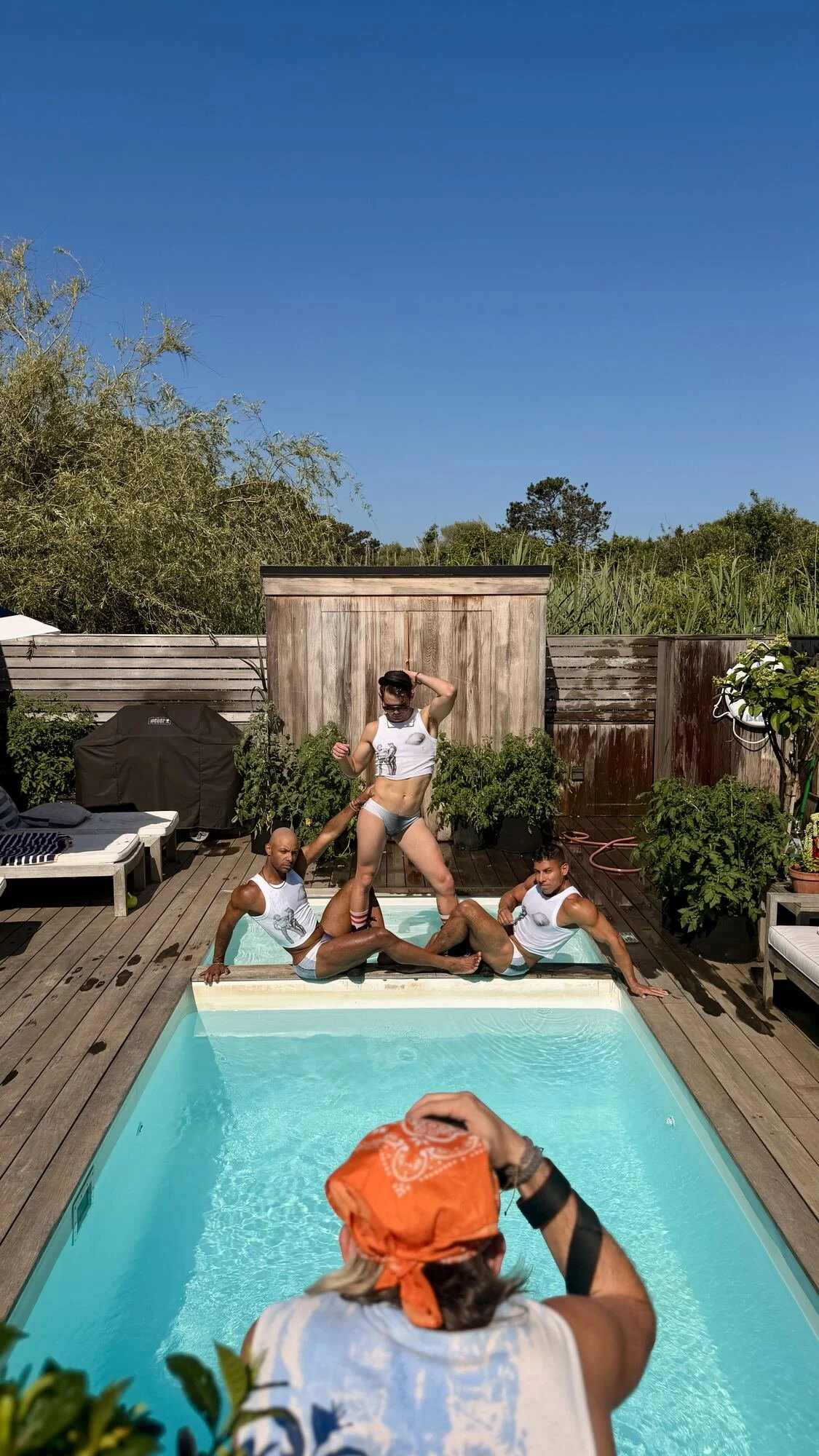Wide shot: pool, sun, the whole crew at work.