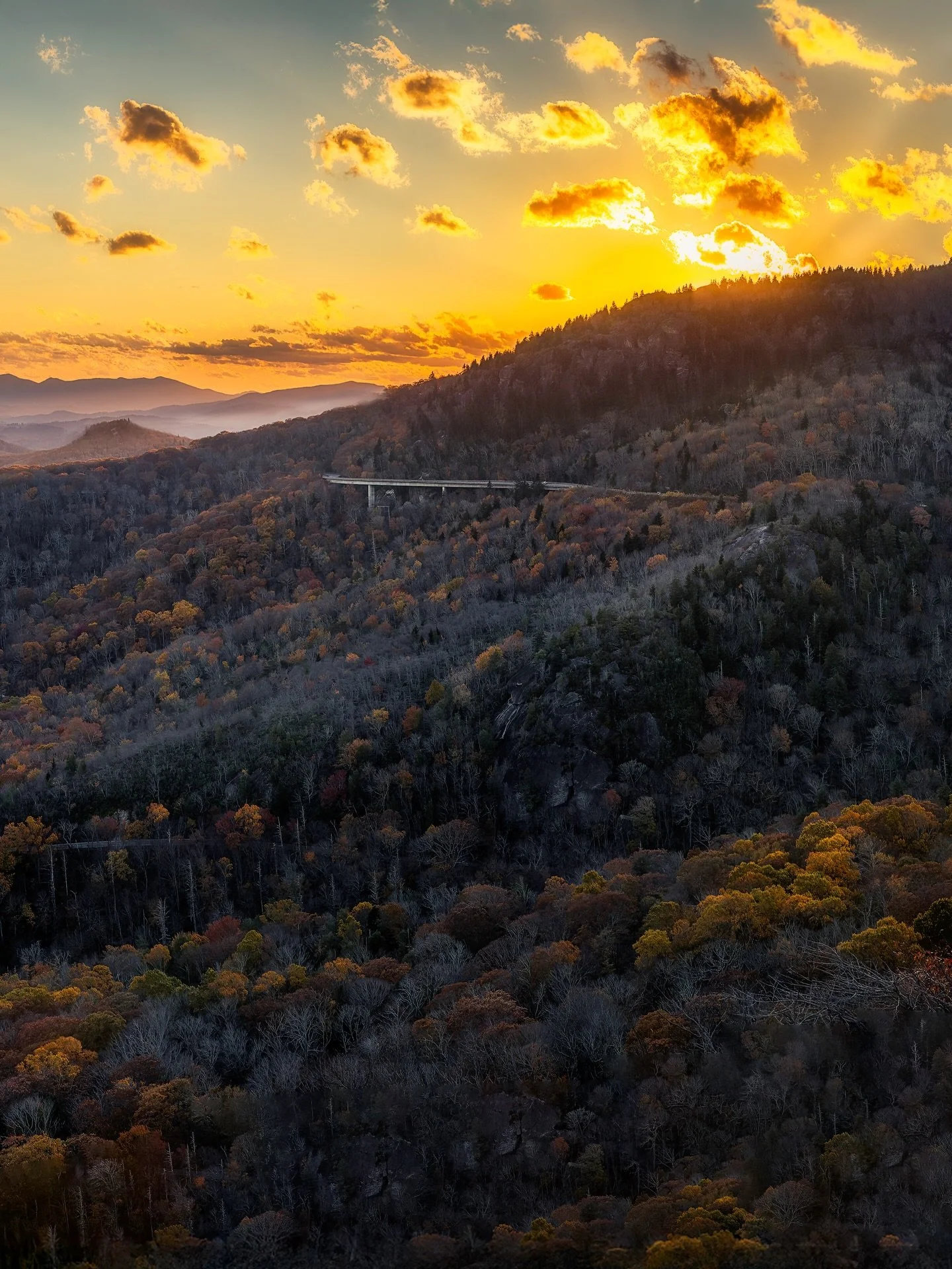 &ldquo;Autumn&rsquo;s Farewell&rdquo;

As the sun sets, dappled golden light kisses the tops of patchy foliage. Clusters of trees line the mountainsides as Autumn draws to a close. Clouds are illuminated with warmth as the last rays disappear behind 