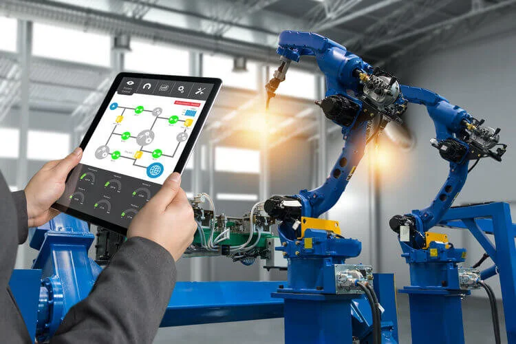 An engineer using tablet, controlling an IOT enabled heavy automation robot arm machine in smart factory industrial with tablet real time process control monitoring system application.