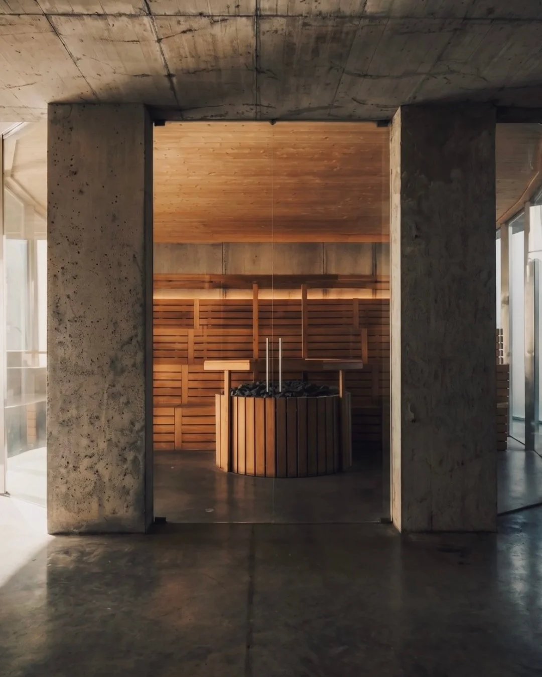 Wooden sauna framed by raw concrete columns at ANTIspa Berlin, combining natural materials with brutalist architecture.