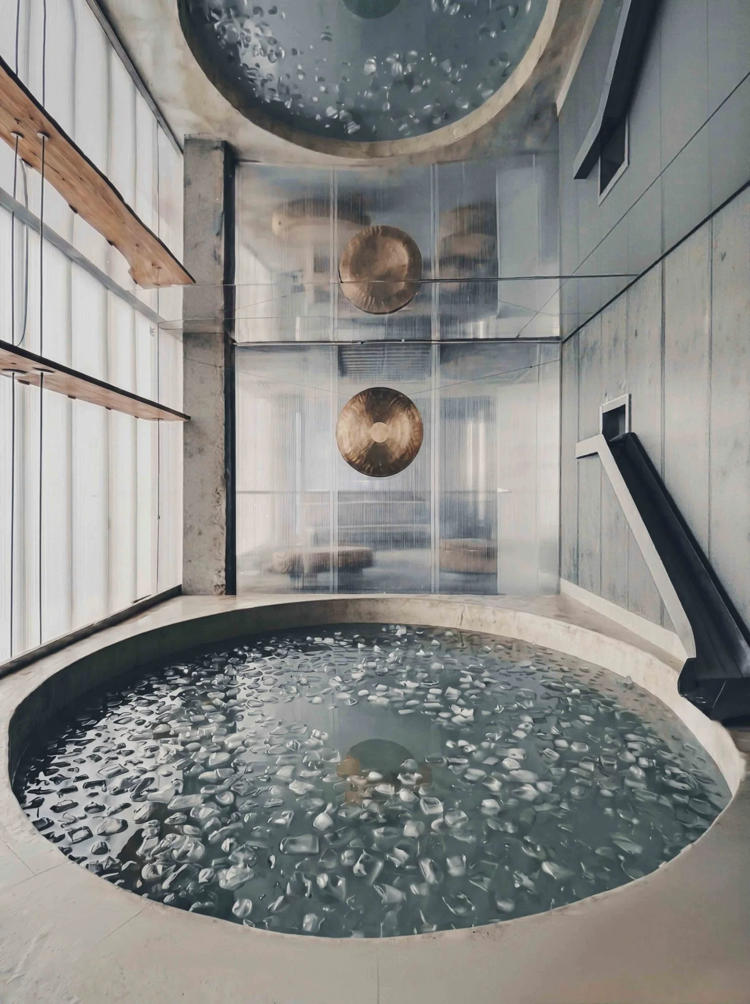 Circular ice bath filled with floating ice cubes at ANTIspa Berlin, surrounded by concrete surfaces, translucent glass and metal gongs.