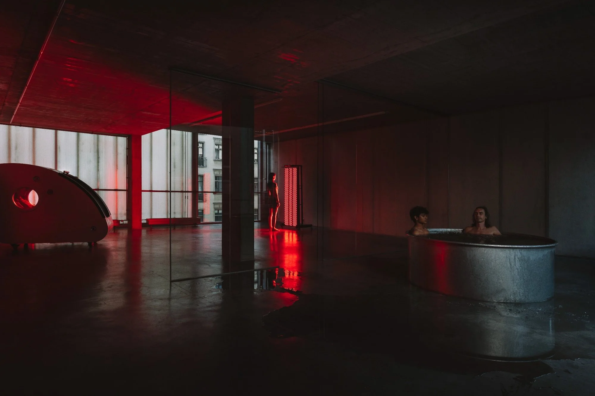 Interior of ANTIspa in Berlin-Mitte, featuring red light therapy, a circular cold plunge pool and exposed concrete architecture.