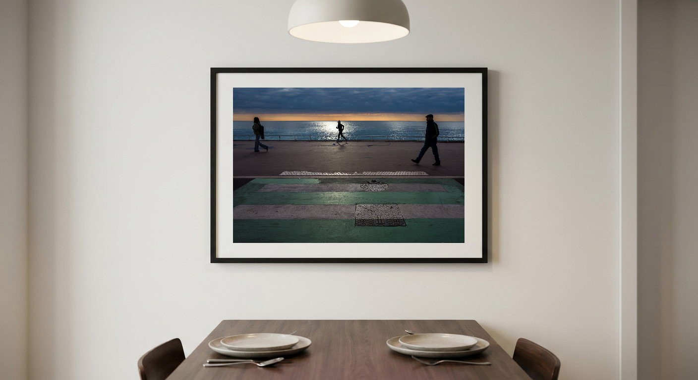 Three silhouetted figures walk on a promenade beside a body of water under a dark cloudy sky. The horizon glows orange and yellow. The promenade is green and gray with white stripes.