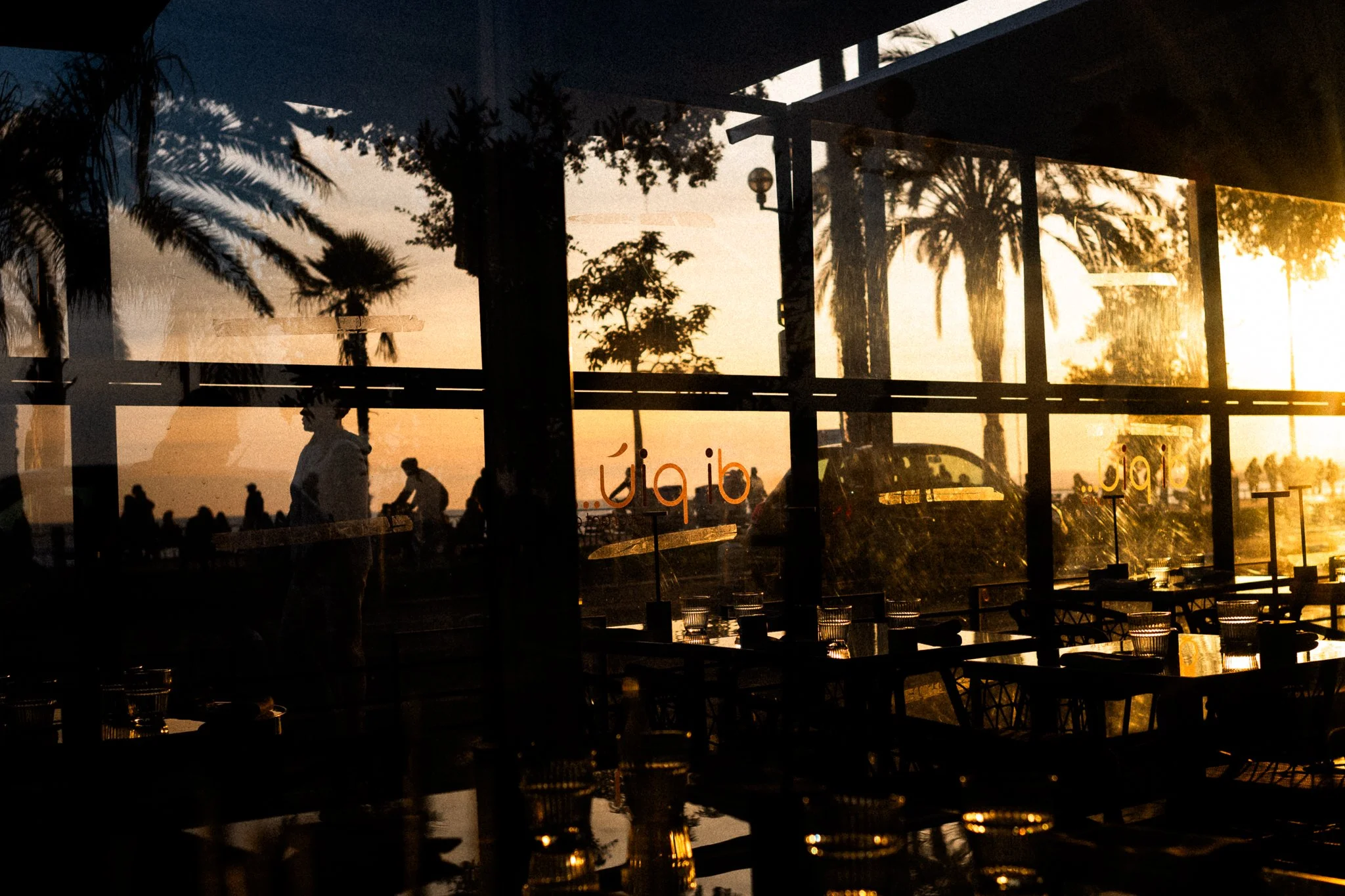 Street photo in Nice on the Promenade des Anglais  golden hour through a glass with silhouettes
