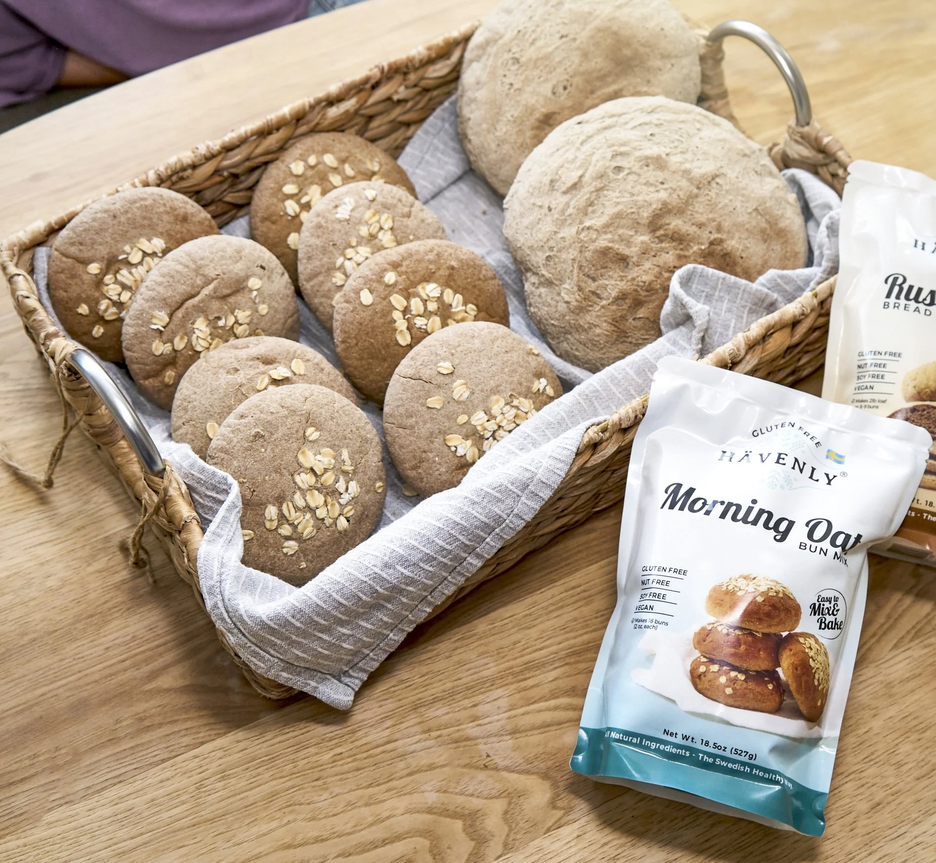 Basket of assorted bread and cookies on a wooden table with a package of multigrain morning oats bun mix.