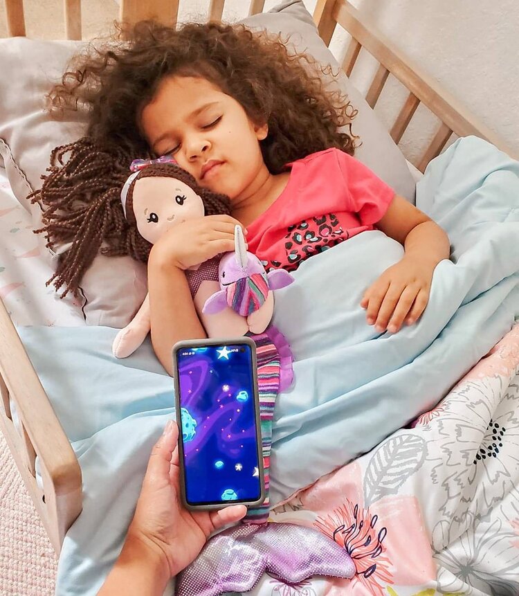 young girl sleeping in crib with moshi app on phone playing above