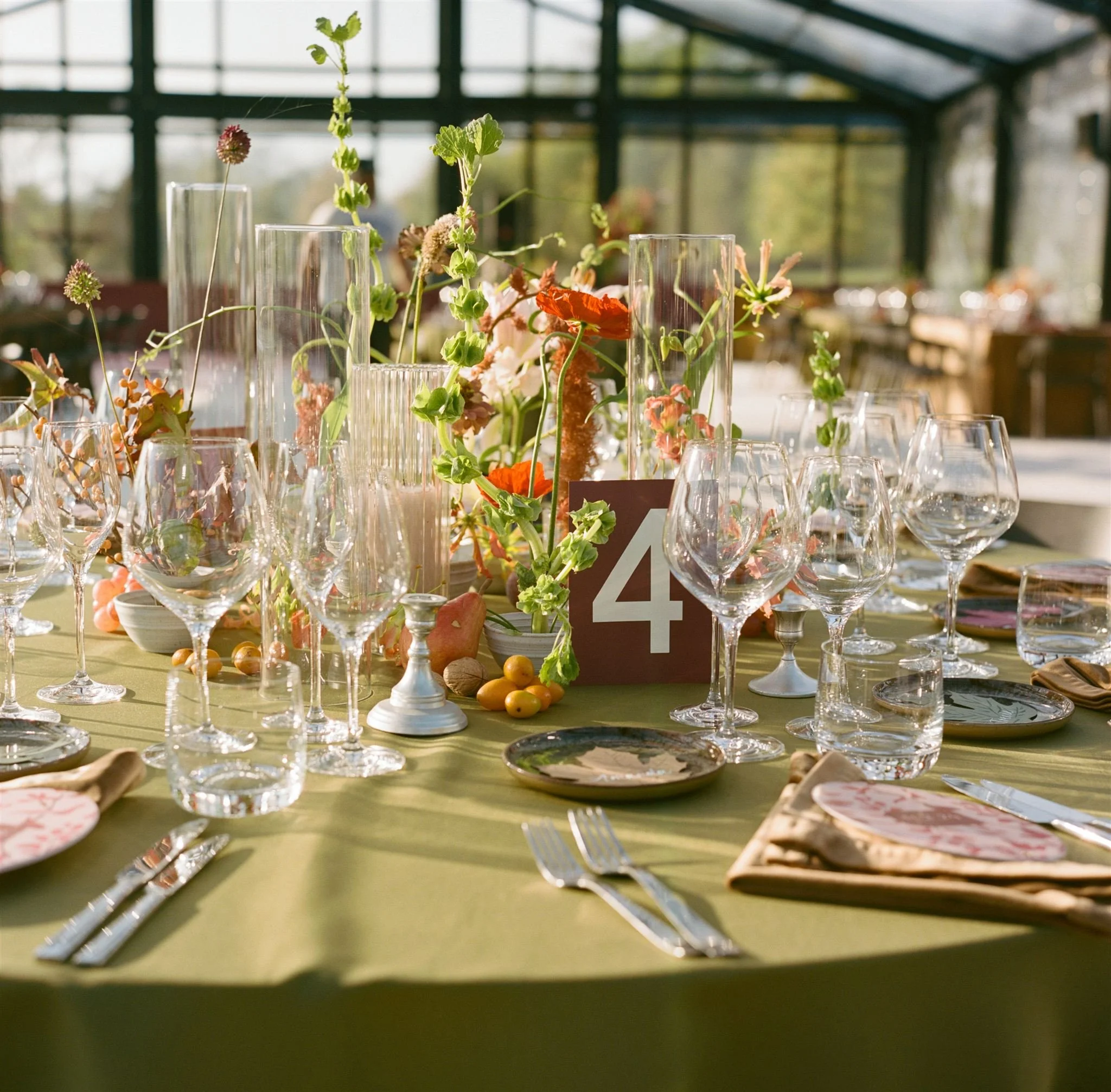Table setup for a formal event with glassware, plates, napkins, and centerpieces of flowers and fruits, with a table number 4 card.