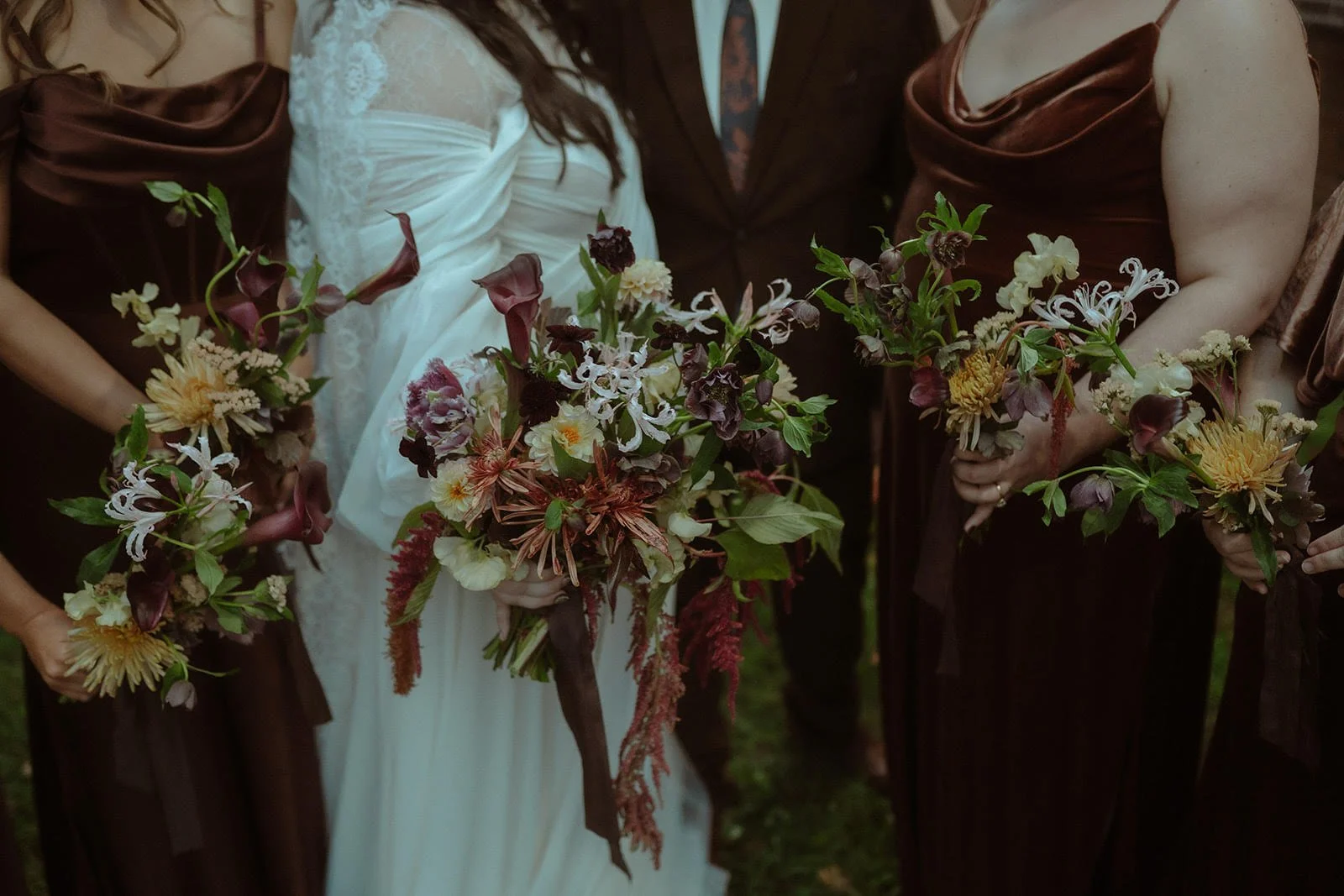 Bridal party holding bouquets, with the bride in white dress and the bridesmaids in brown dresses.
