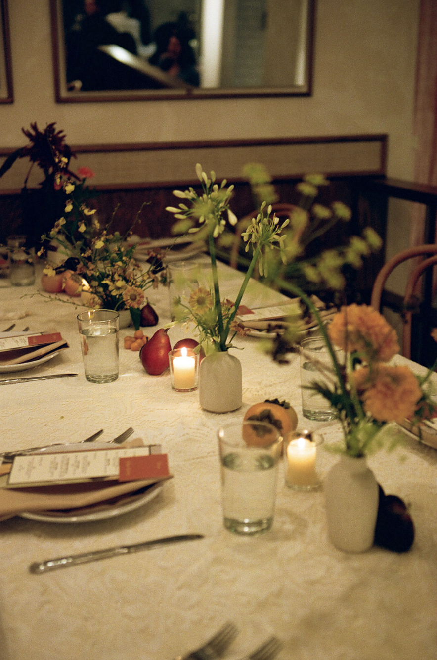 A decorated dinner table with floral arrangements, lit candles, glasses of water, and place settings, set for a meal in a warmly lit room.