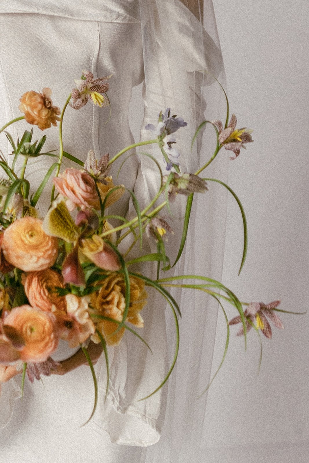 A bouquet of peach and pink flowers with greenery, partially wrapped in transparent white paper, resting on a surface.