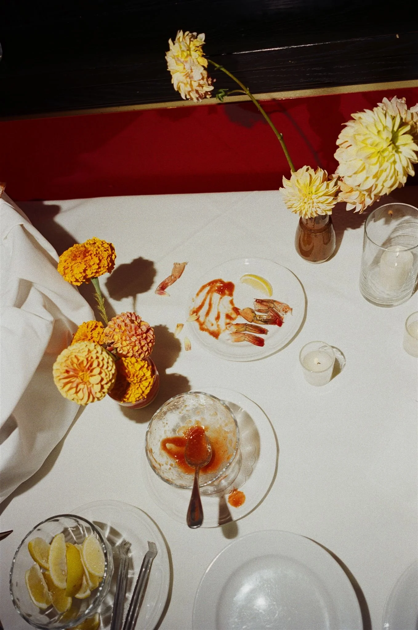 Empty seafood plates with shrimp shells, lemon slices, and red sauce, surrounded by flowers in vases on a white table at a restaurant.