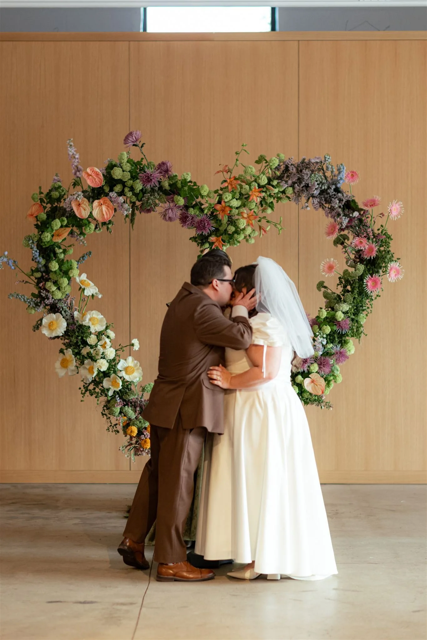 A bride and groom sharing a kiss in front of a heart-shaped floral arch during their wedding ceremony.