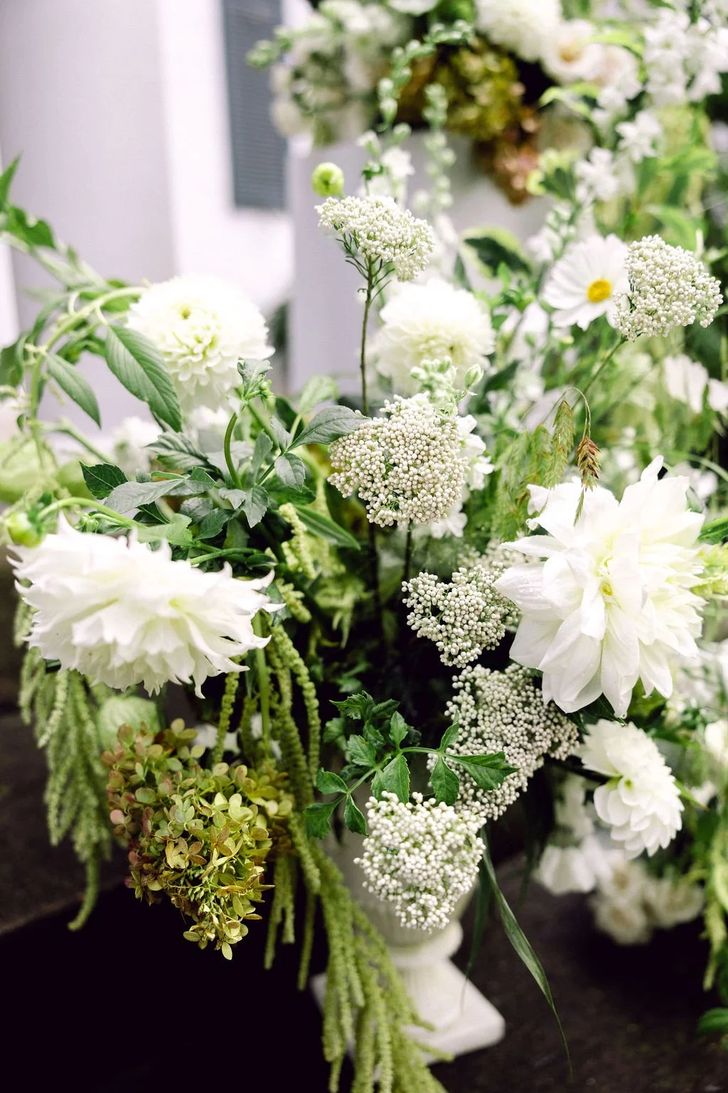A bouquet of white flowers including dahlias, clematis, and hydrangeas in a white vase.