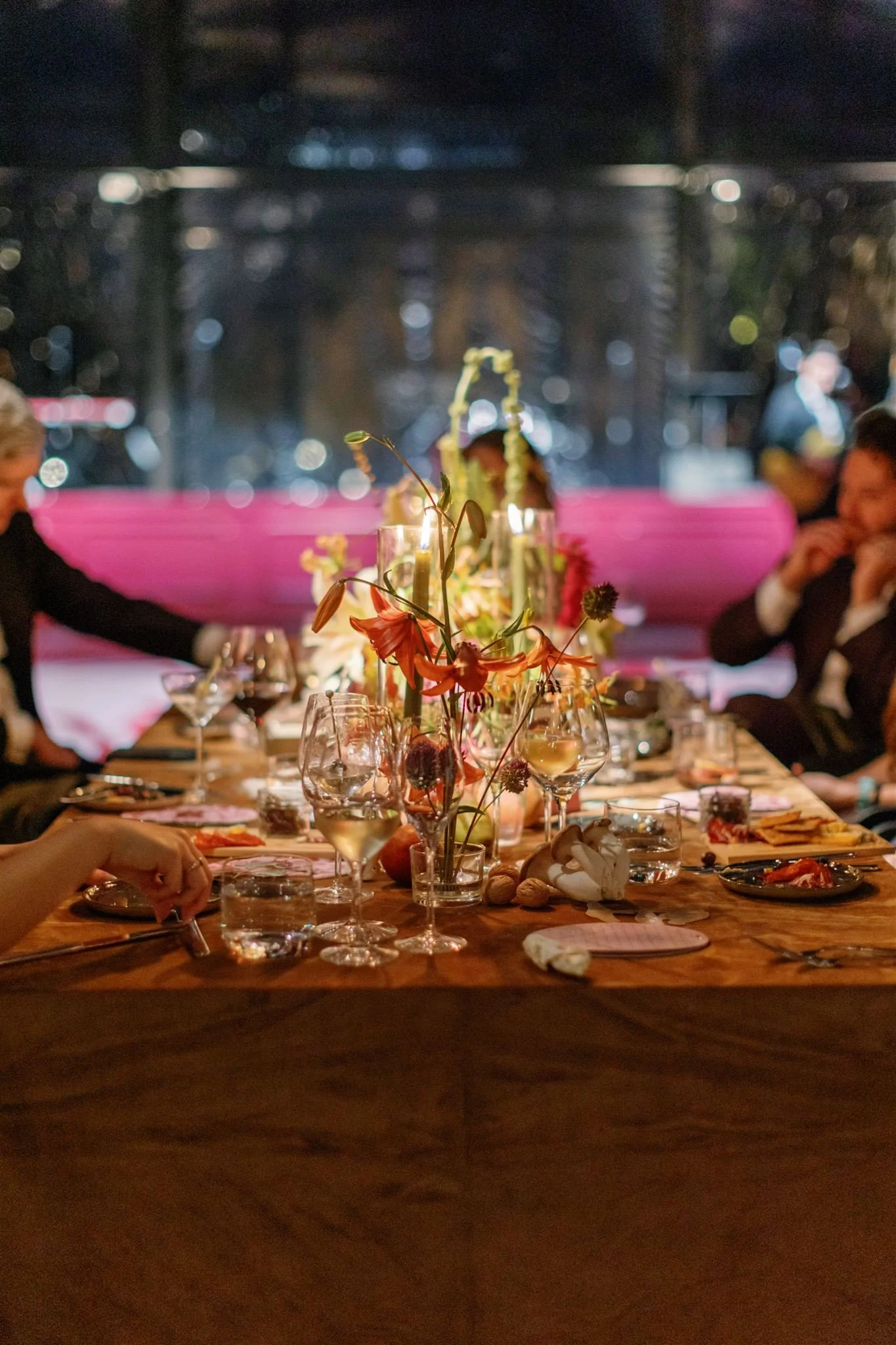 A dinner party table with floral centerpieces, glassware, and place settings in a dimly lit room.