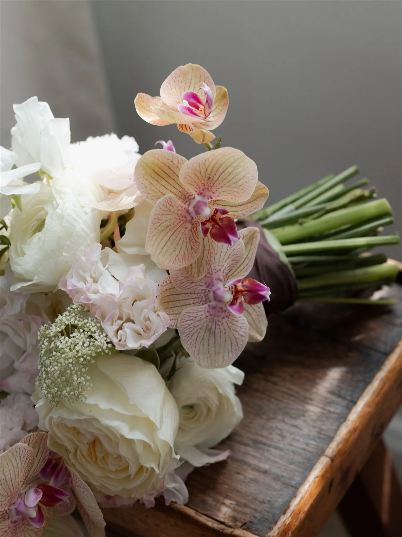 A bouquet of various white and pink orchids and flowers resting on a wooden surface.