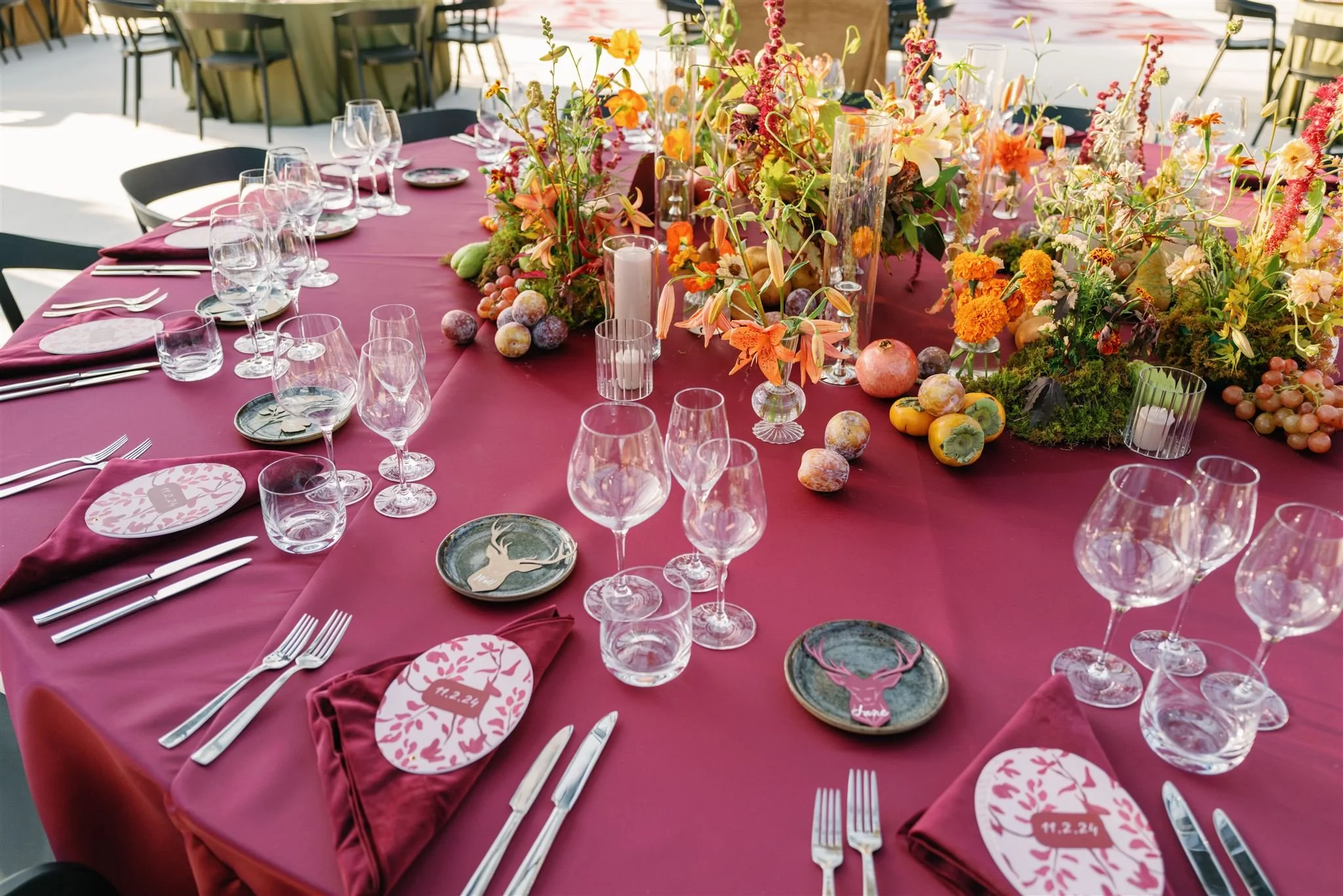 A decorated banquet table with a pink tablecloth, floral centerpiece, multiple wine glasses, silverware, napkins, and decorative plates with stag designs.