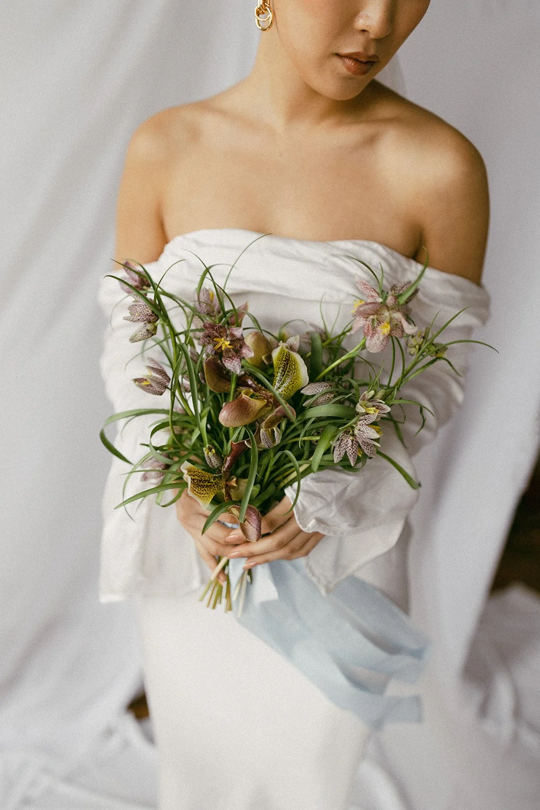Woman in off-shoulder white dress holding a bouquet of pink and yellow orchids
